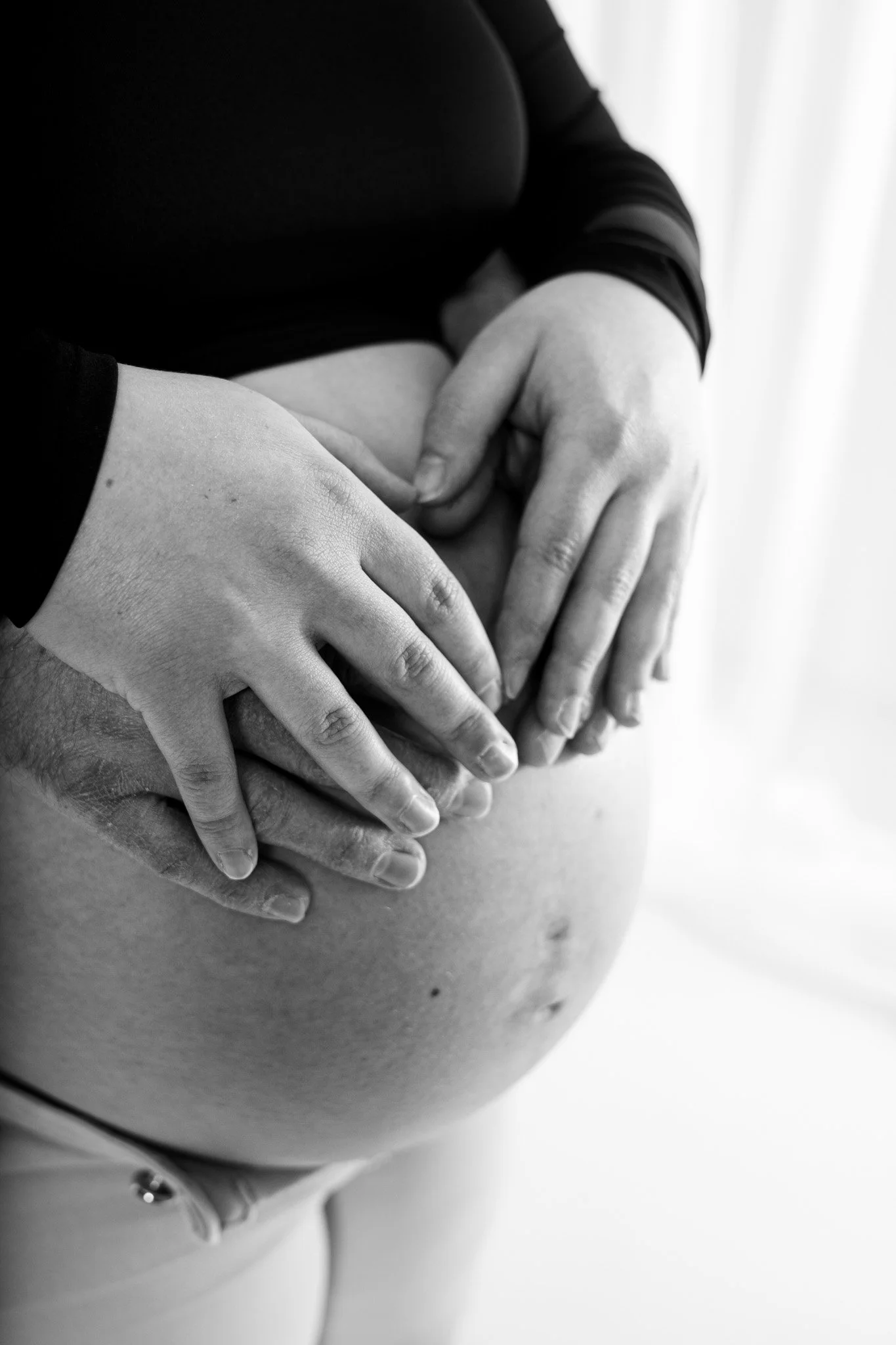 Zwart-wit foto van een zwangere buik met twee paar handen die de buik vasthouden.