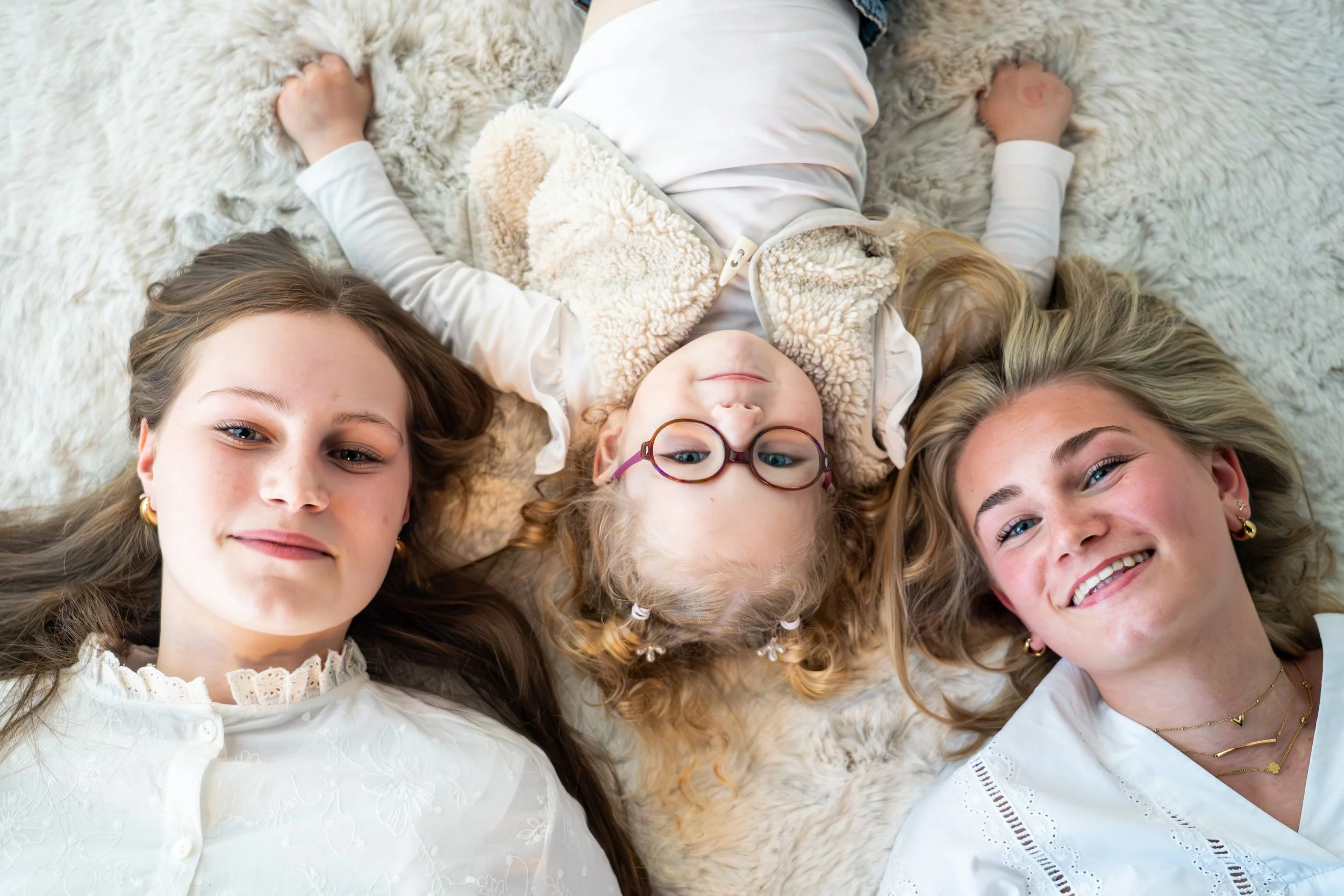 Drie vrouwen en een jong meisje liggen op een zachte ondergrond, glimlachen en kijken naar de camera.