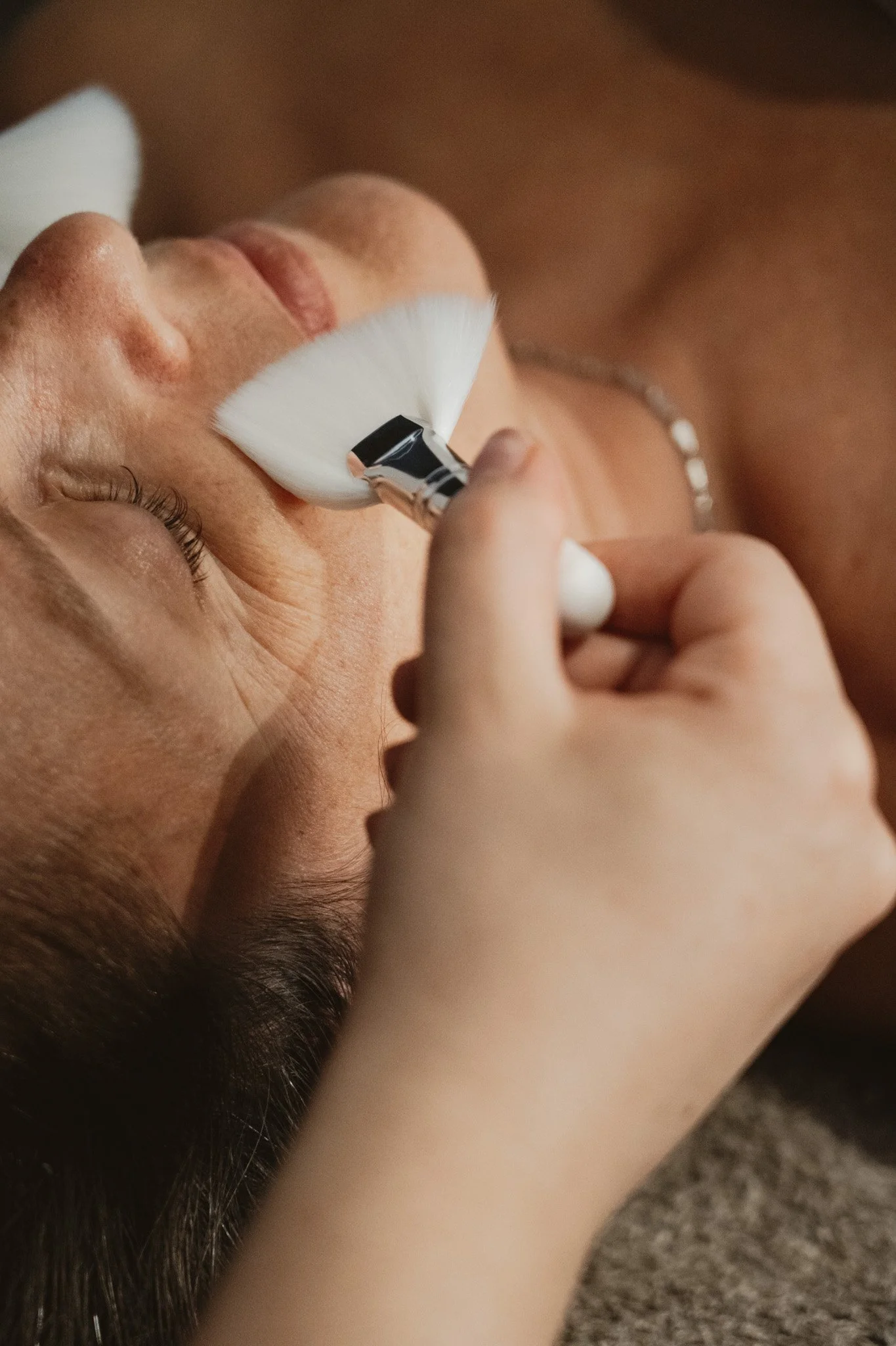 Close-up van een persoon die een make-up borstel op het gezicht aanbrengt terwijl ze met haar ogen dicht liggen.