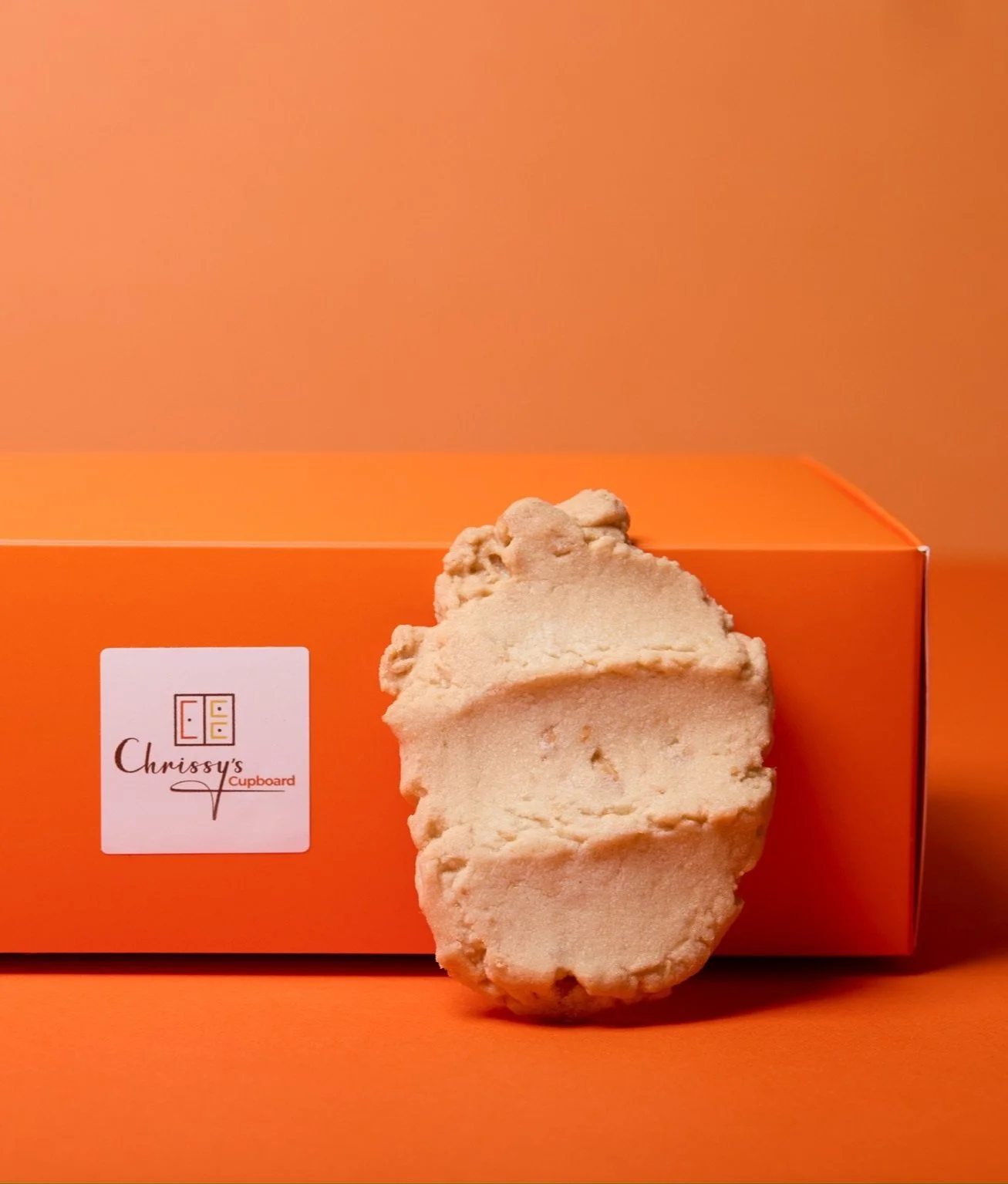 Individual Macadamia Cookie leaning against orange Chrissy's Cupboard box