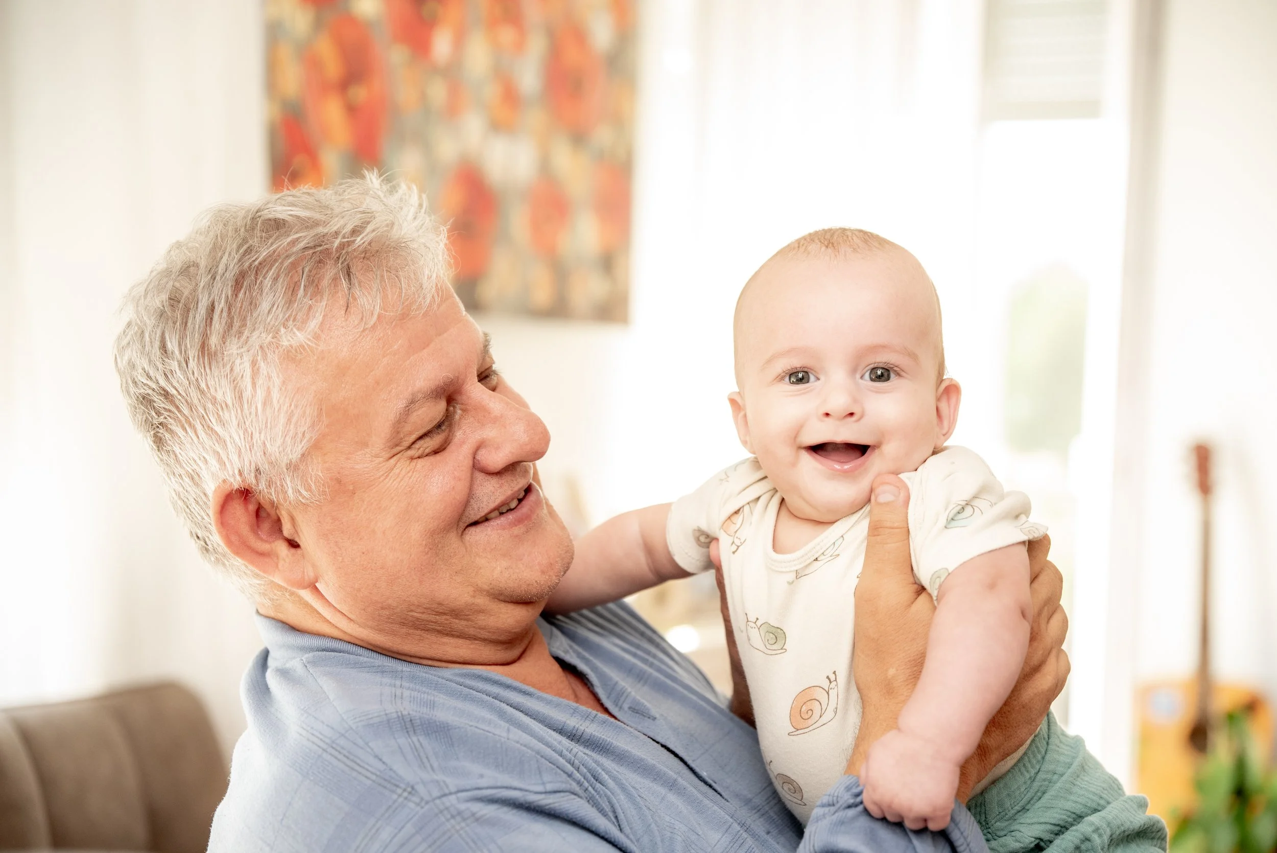 Elderly man holding a smiling baby indoors.