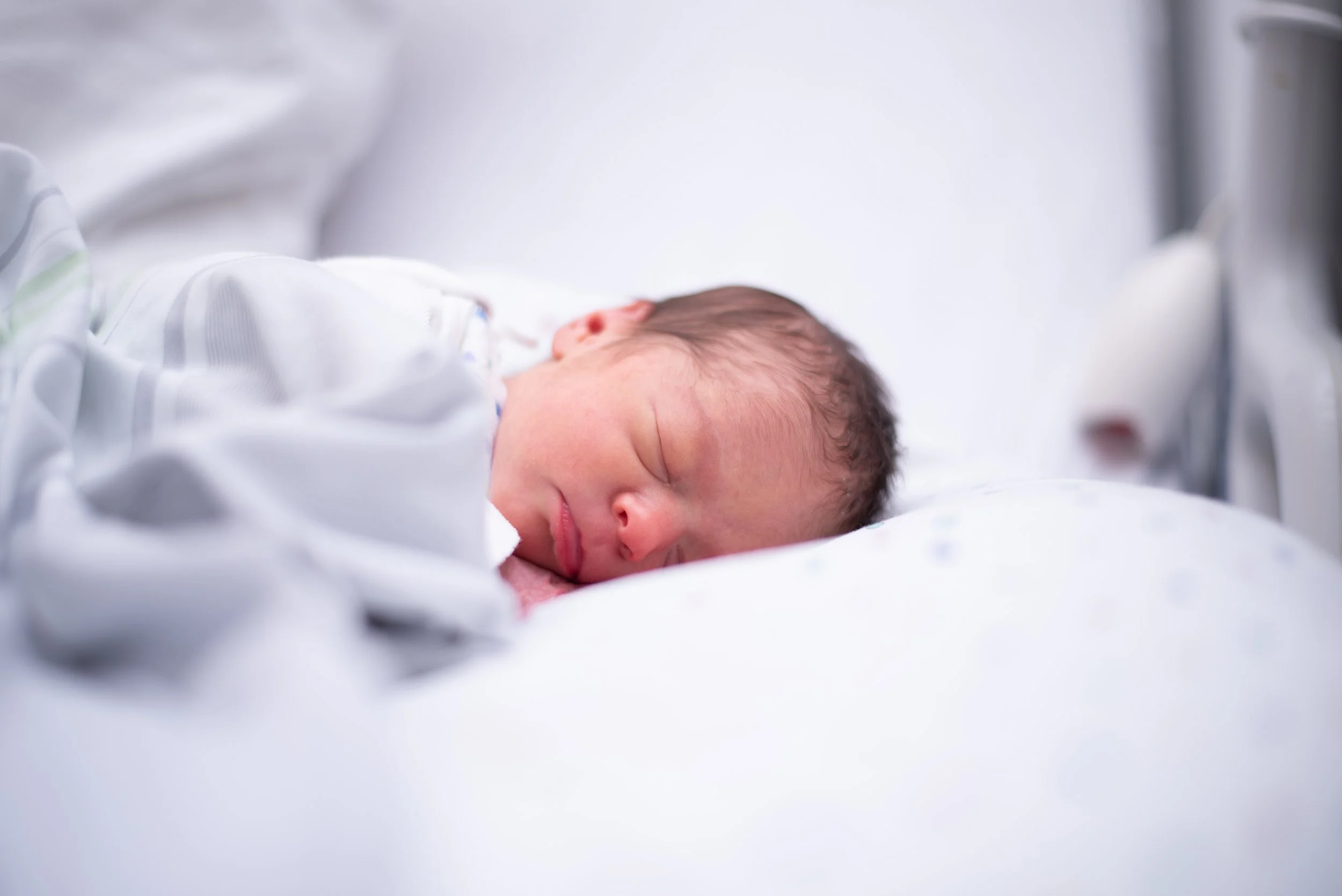 Newborn baby sleeping in a hospital bed with a white blanket.