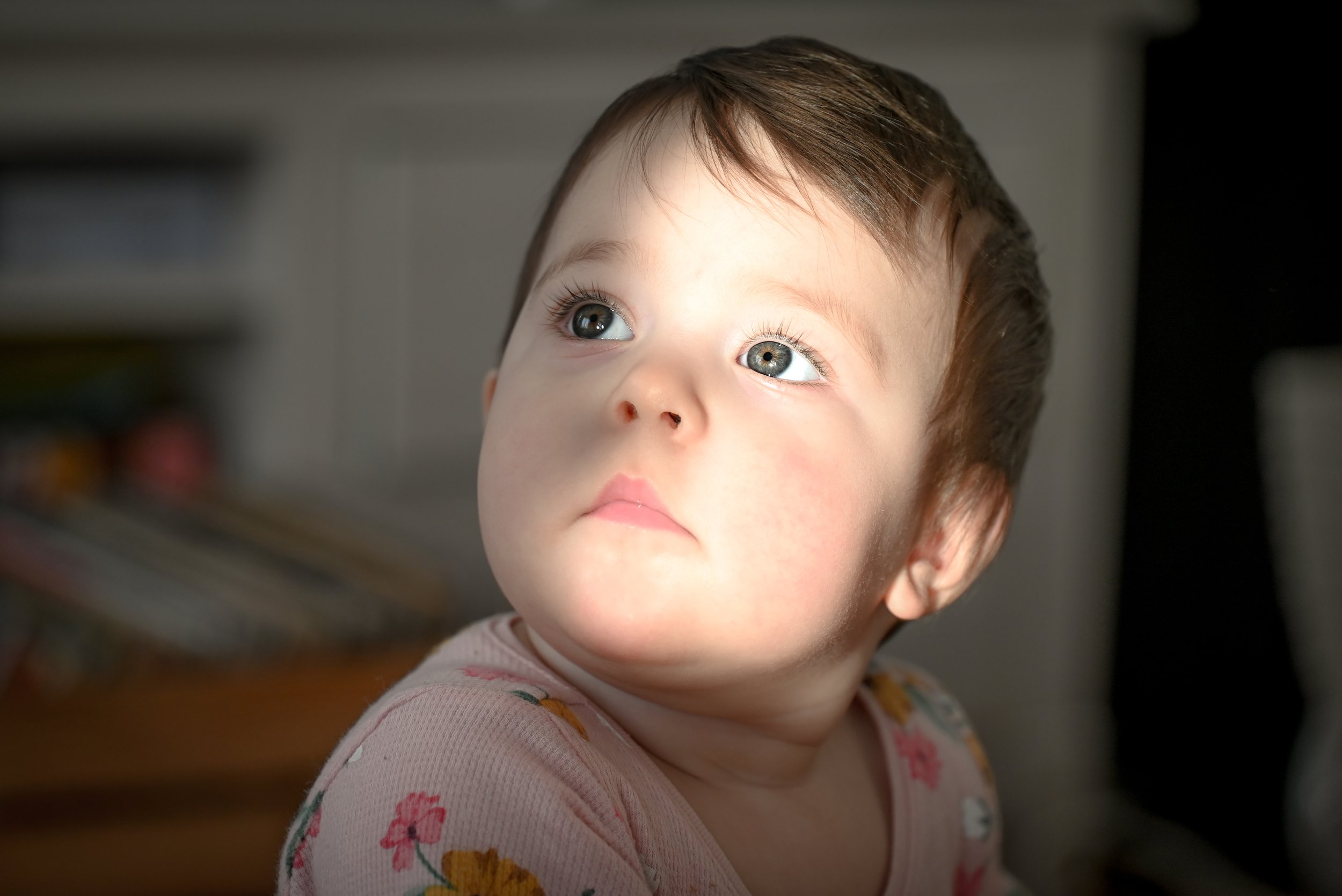 Close-up of a baby with blue eyes and a floral-patterned outfit, looking upwards.