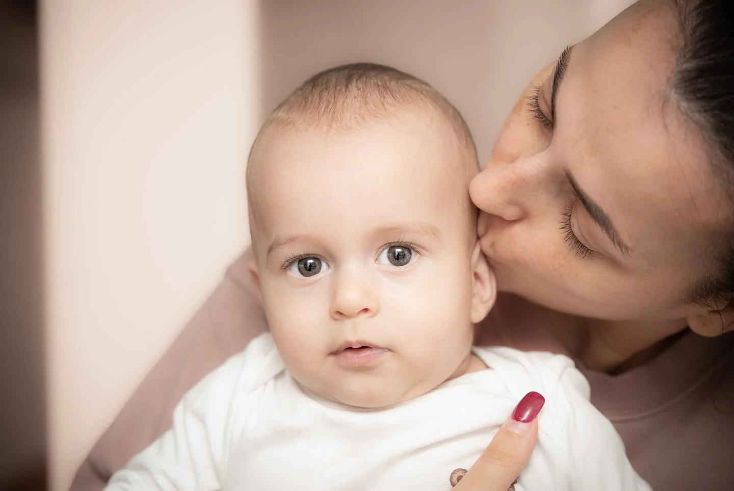 A woman kissing a baby on the cheek, baby looking at camera.