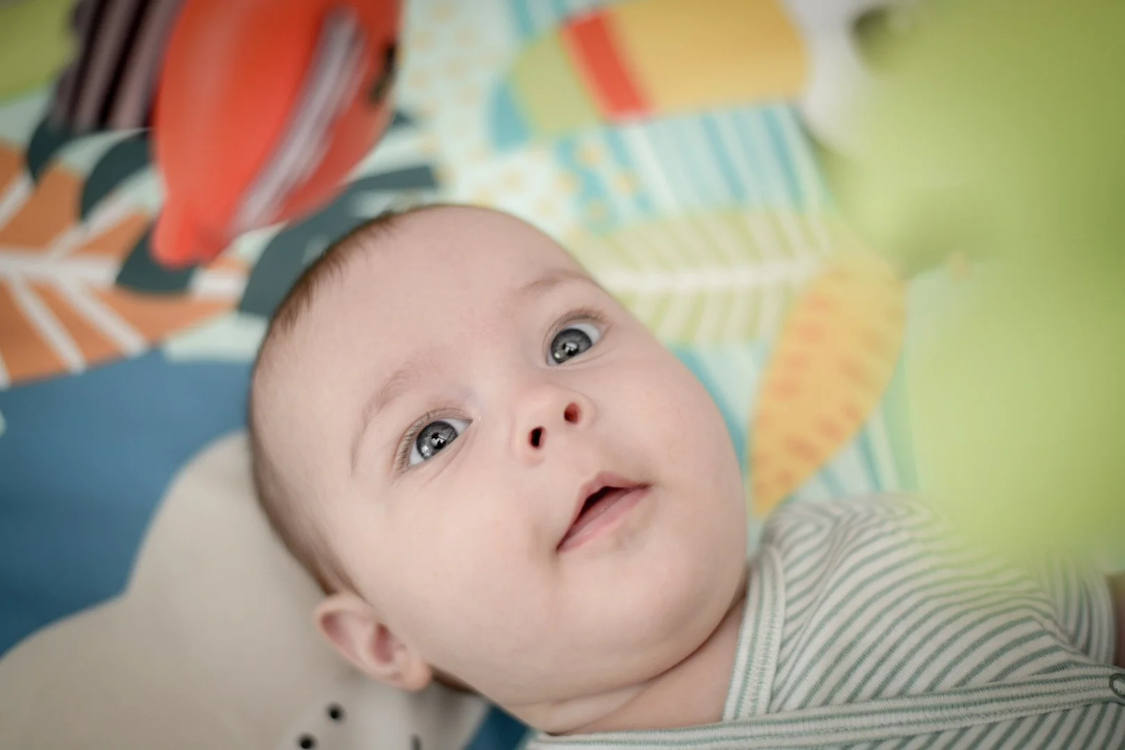 Baby lying on a colorful play mat, looking upwards.