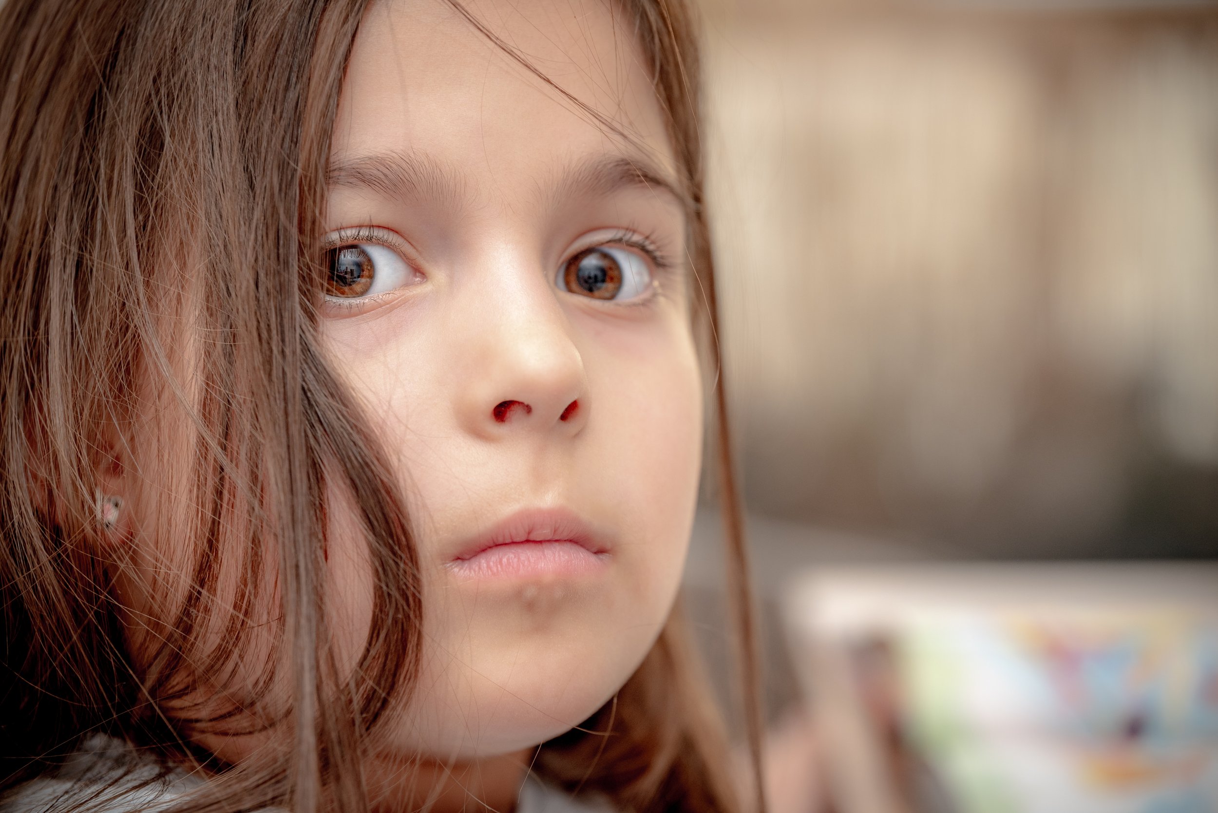 Close-up of a young girl with long brown hair and wide, expressive eyes looking towards the camera.