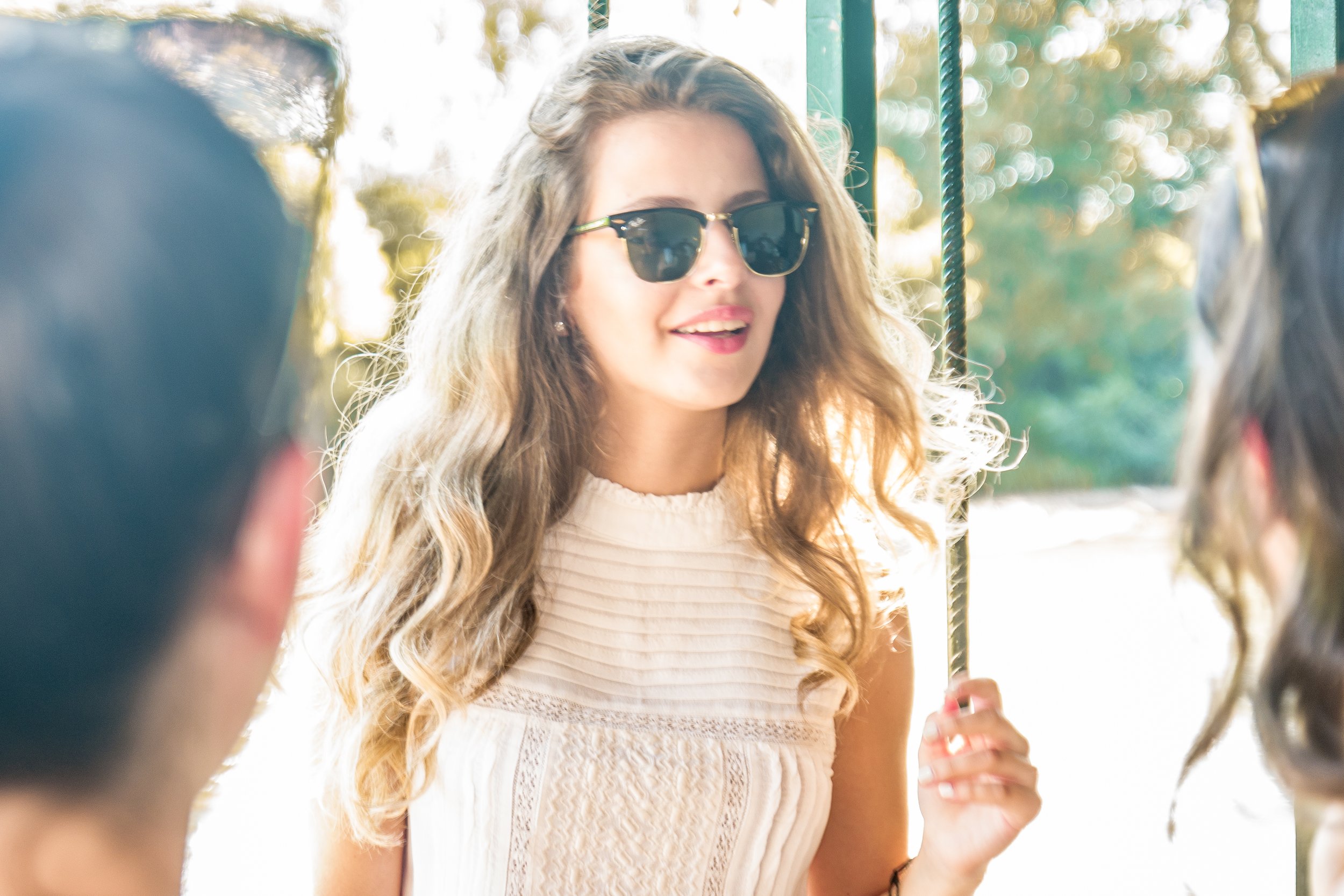Woman with blonde hair and sunglasses smiling outdoors in sunlight.