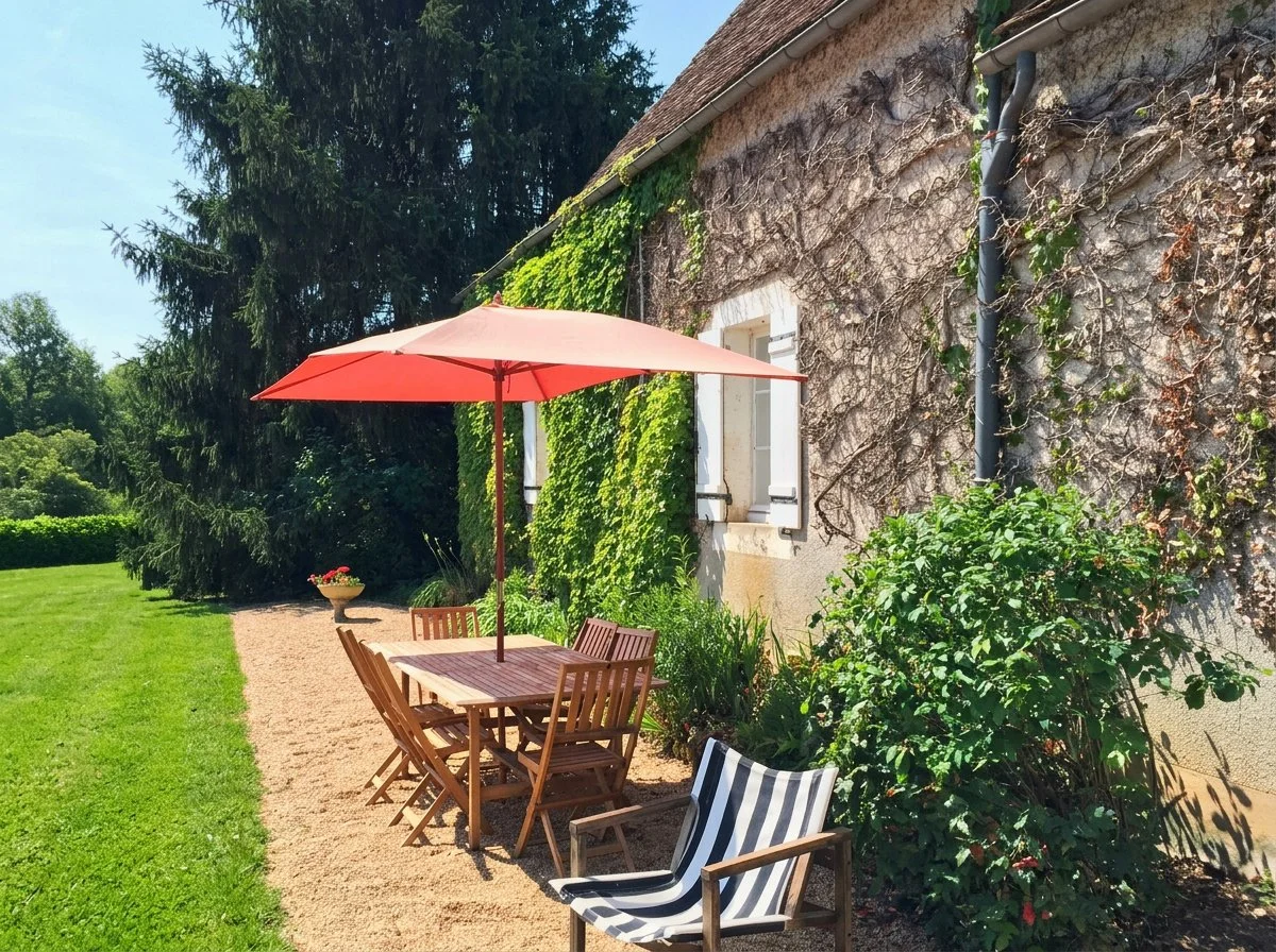 Wooden table and chairs outside in garden at Domaine de Tabary with red umbrella up for shade