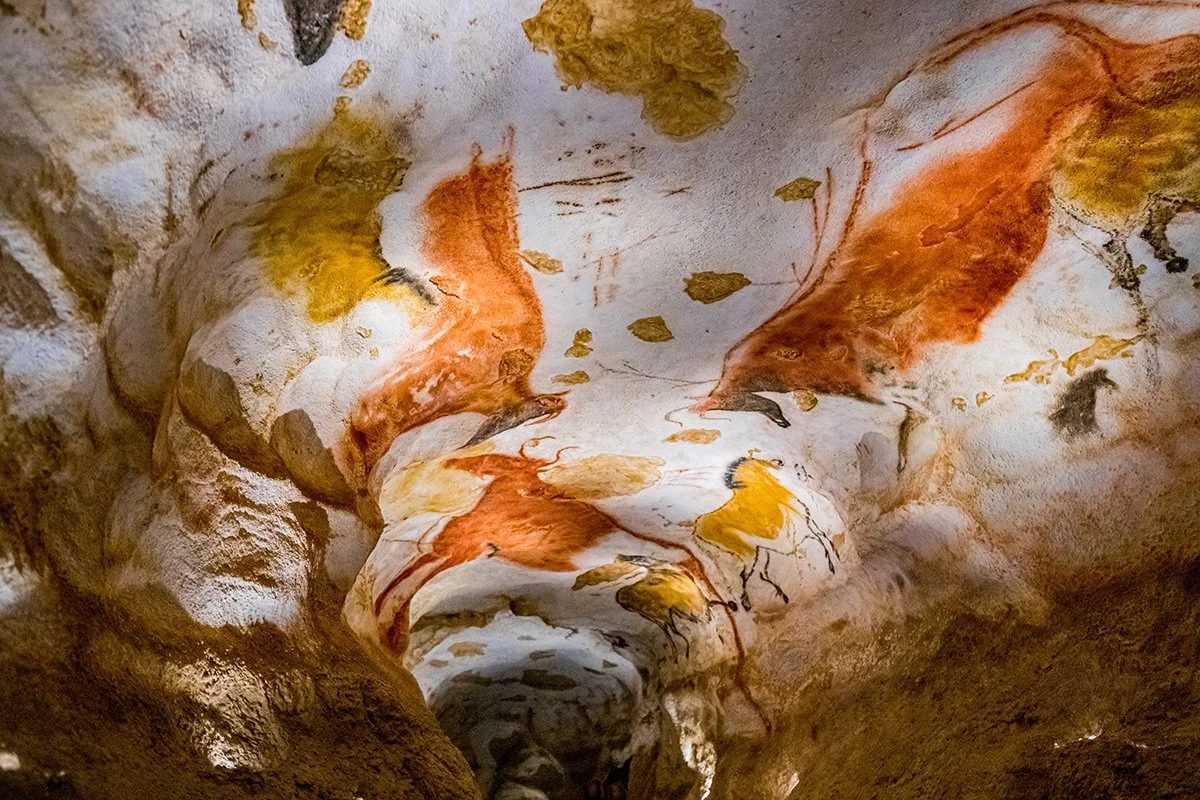 Cave interior with painted cave art of yellow and red animals.