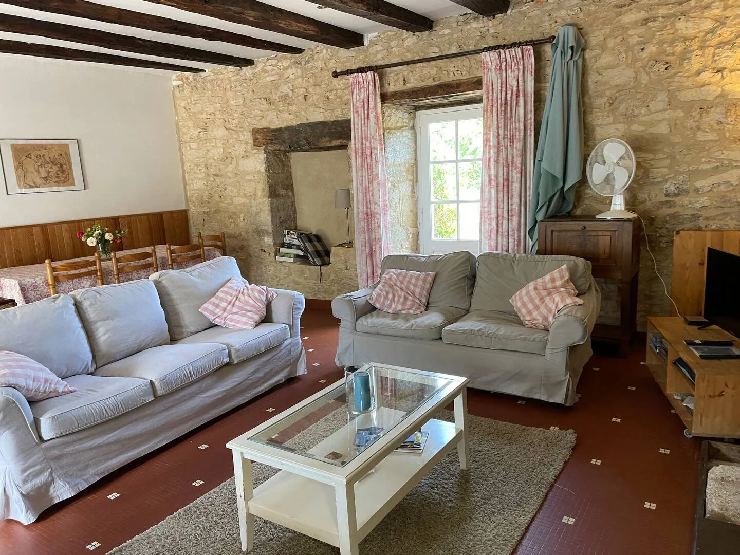 Living room in Tabary Farmhouse with stone wall, wooden beams, sofas and a glass coffee table