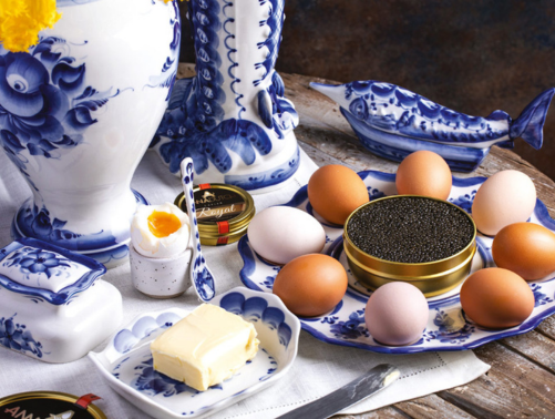 Blue and white porcelain vases, a fish-shaped dish, and a plate with brown and white eggs and a spoonful of butter on a wooden table.