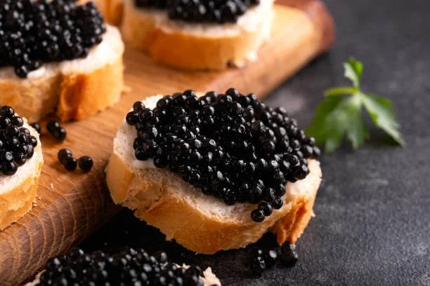 Slices of baguette bread topped with butter and black caviar, garnished with a sprig of parsley.