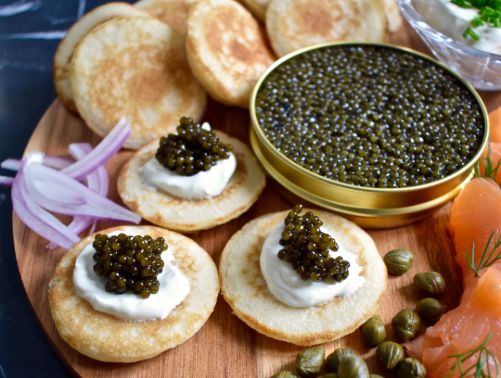 Appetizer plate with toasted bread rounds topped with sour cream and caviar, served with sliced red onions and garnishes.