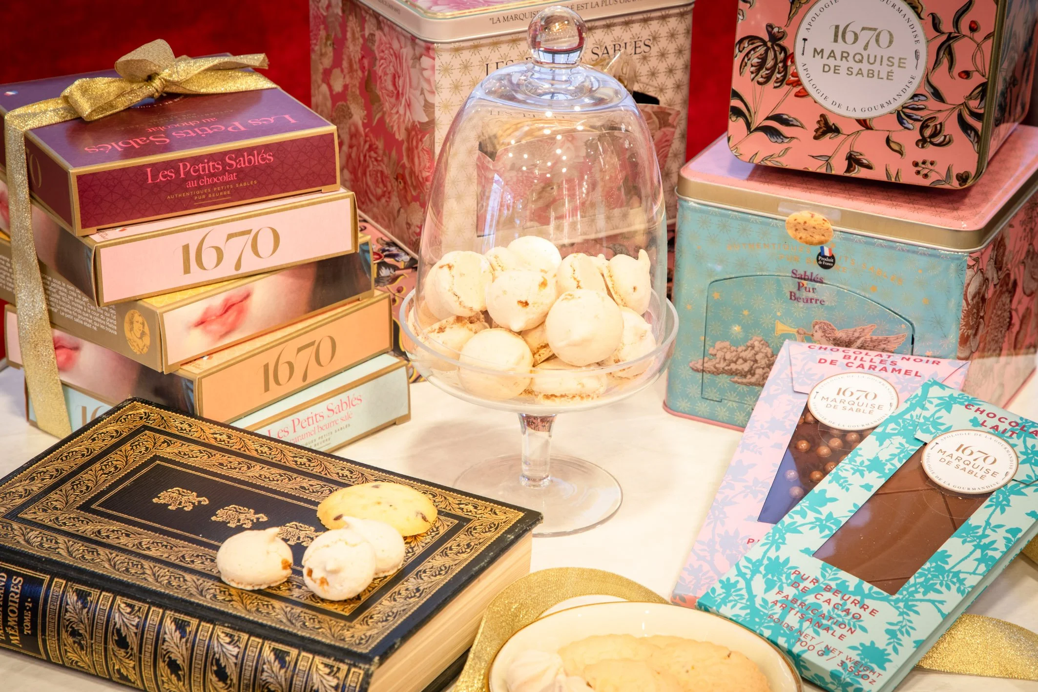 A collection of decorative candy and cookie boxes, a glass dome with macarons, and assorted chocolates on a table