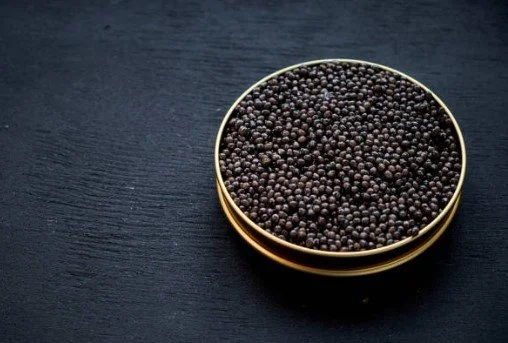 A round, gold-colored container filled with black caviar imperia placed on a dark wooden surface.