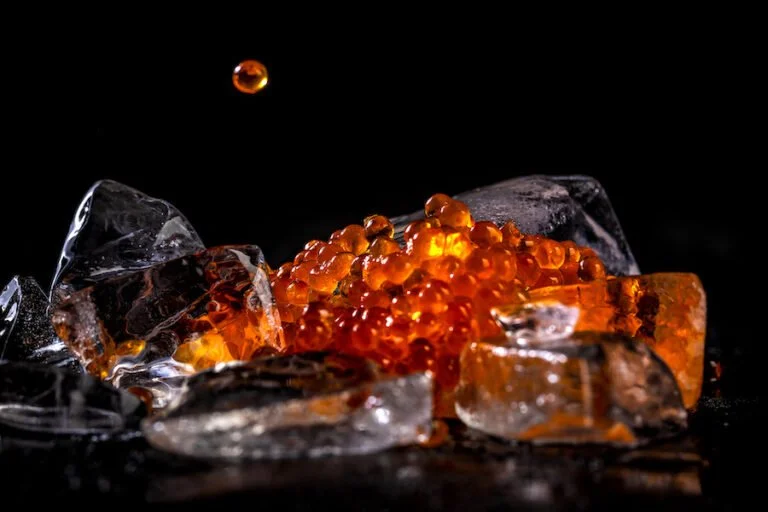 Ice cubes with orange fish roe caviar on top against a black background