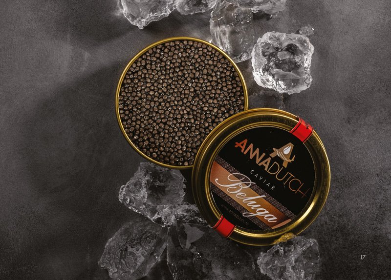 An open tin of Anna dutch caviar on a dark surface surrounded by ice cubes.