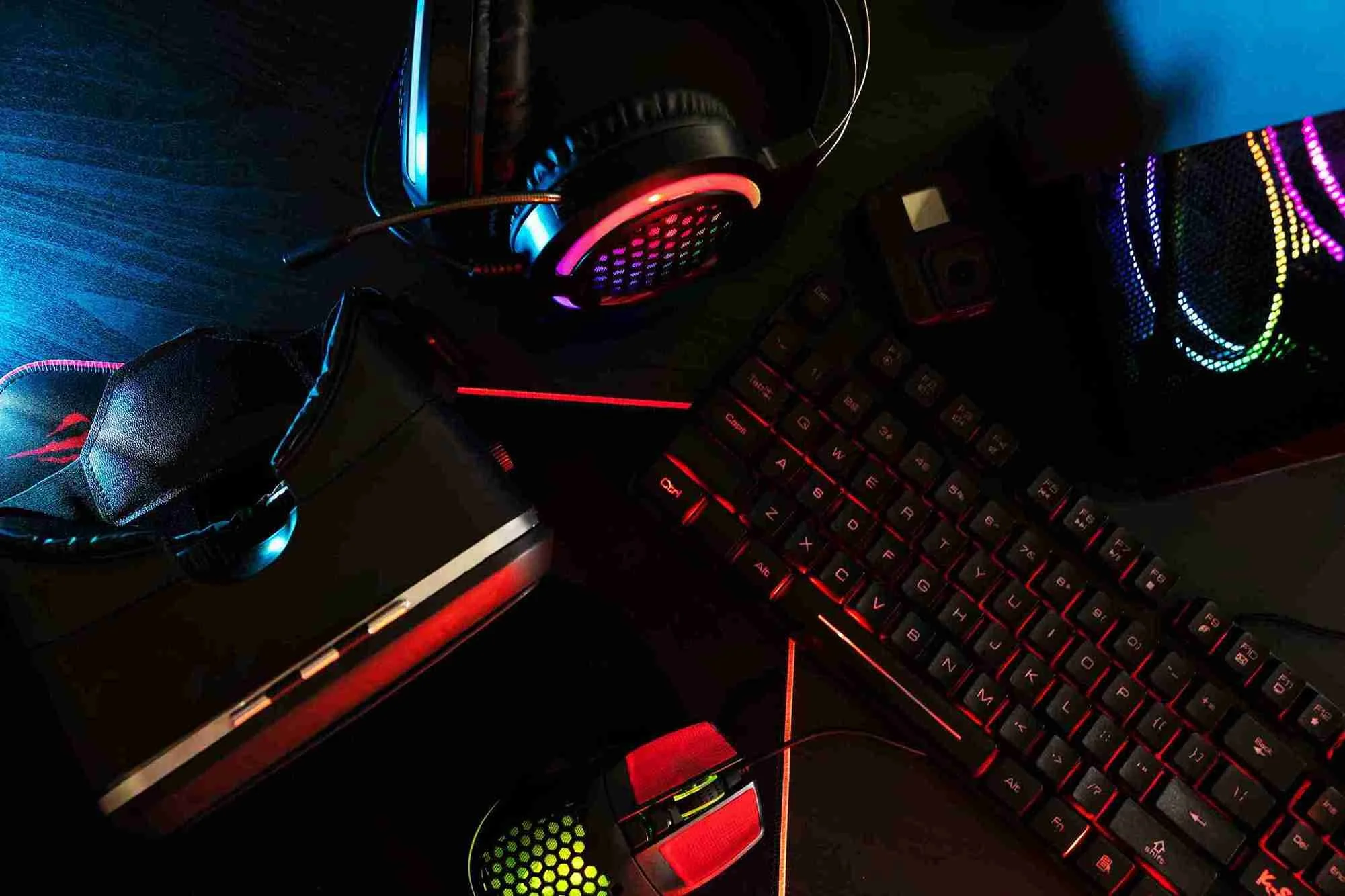PNS777 - Gaming setup with headphones, keyboard, mouse, and VR headset on a dark desk with colorful LED lighting.