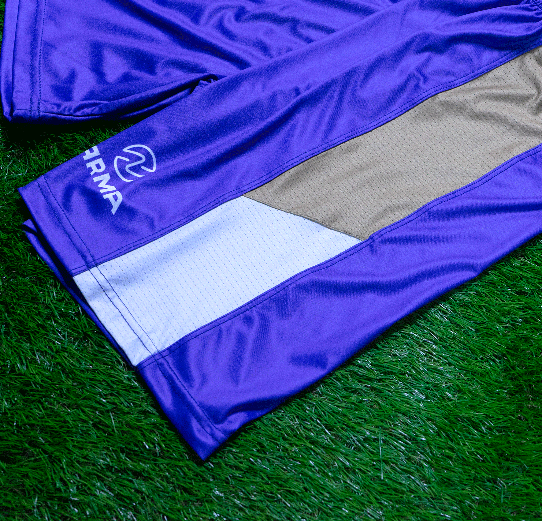 Close-up of a sports jersey laid on green artificial grass, purple and gray colors, with a logo and text on the sleeve reading 'TRAI'}