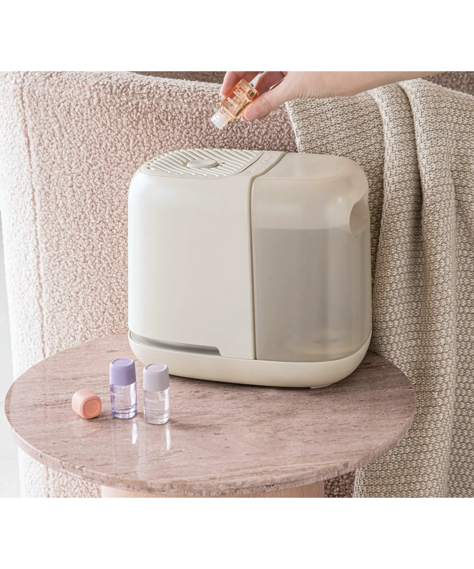 canopi humidifier with three essential oils and a hand adding drops of essential oil to humidifier