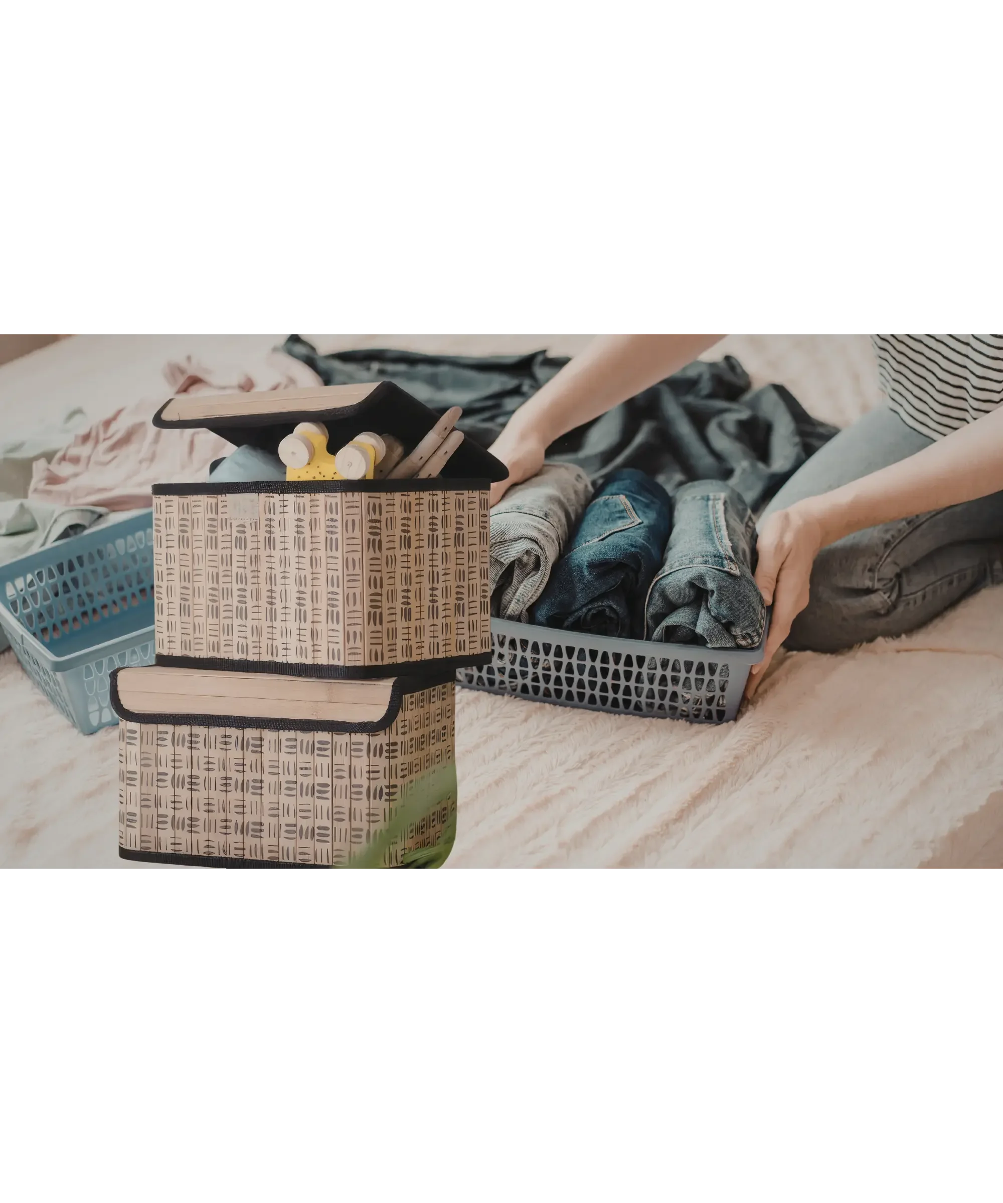 Person organizing folded jeans and clothing into storage baskets on a bed, with fabric storage boxes and neatly arranged items in a cozy home setting.