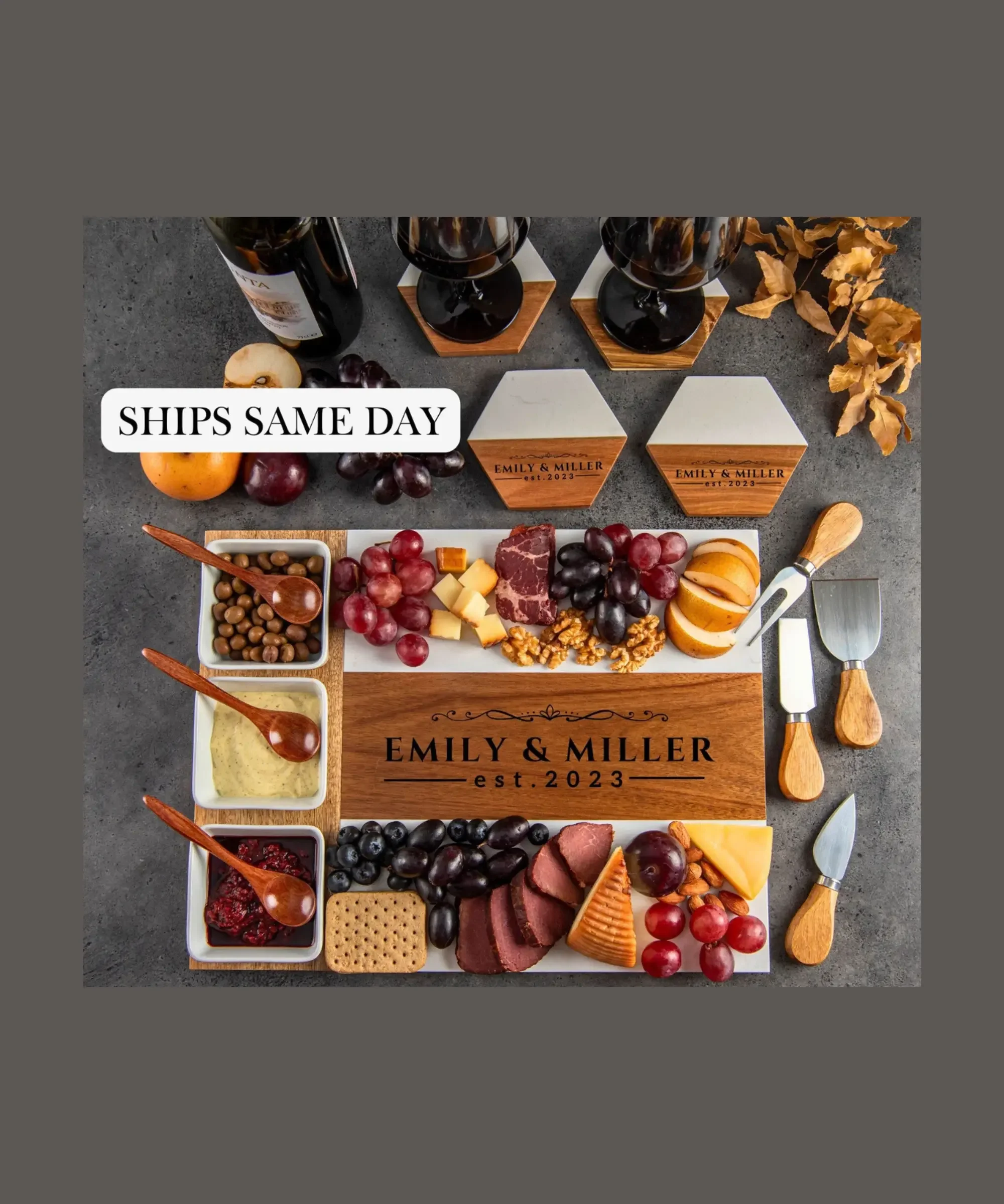 Personalized charcuterie board gift set engraved with names and date, wooden cheese board with wine glasses, cheeses, grapes, and serving utensils.