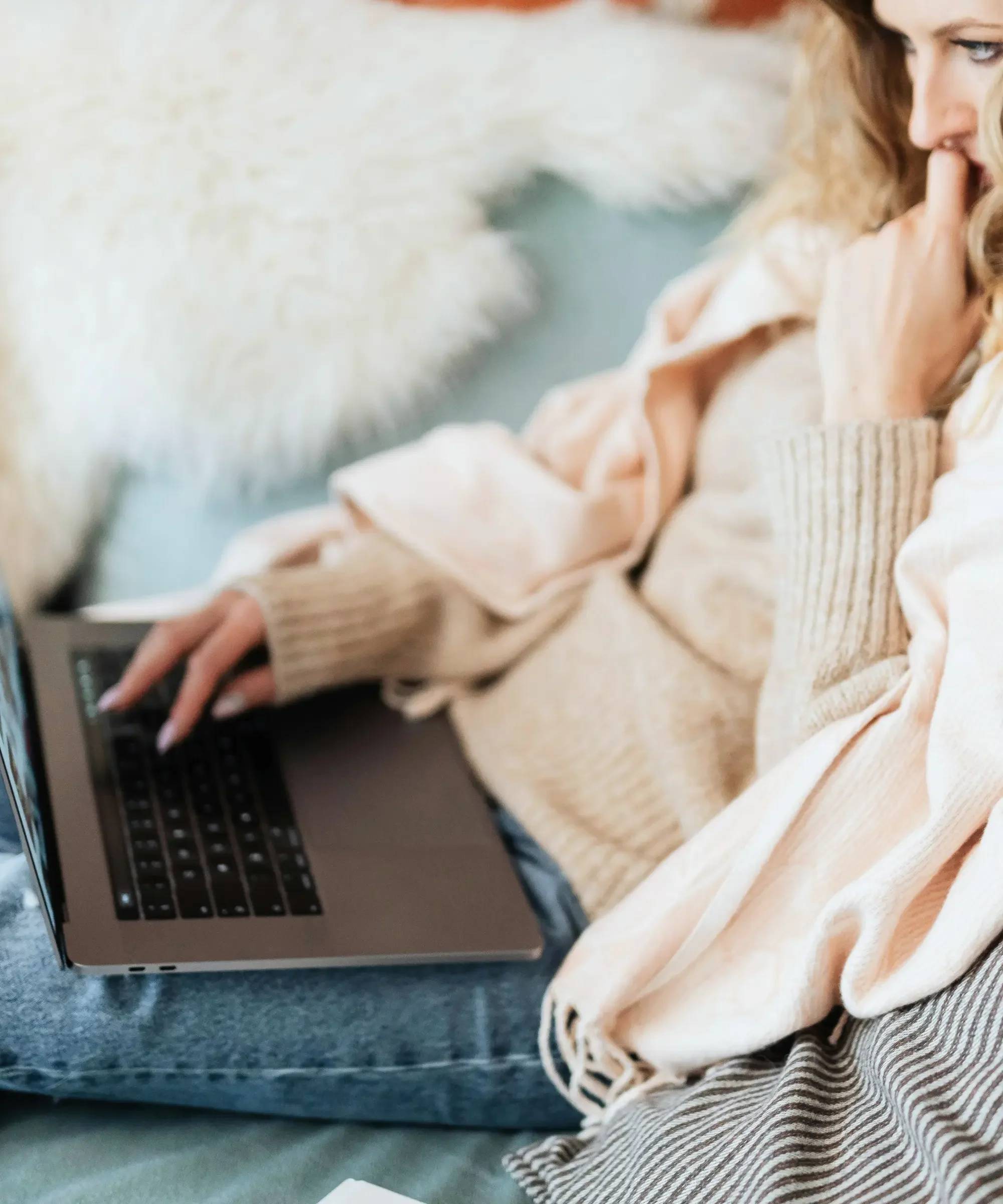 Woman over 40 sitting on a couch using a laptop, appearing thoughtful and reflective, symbolizing midlife stress, overthinking, and emotional overload.