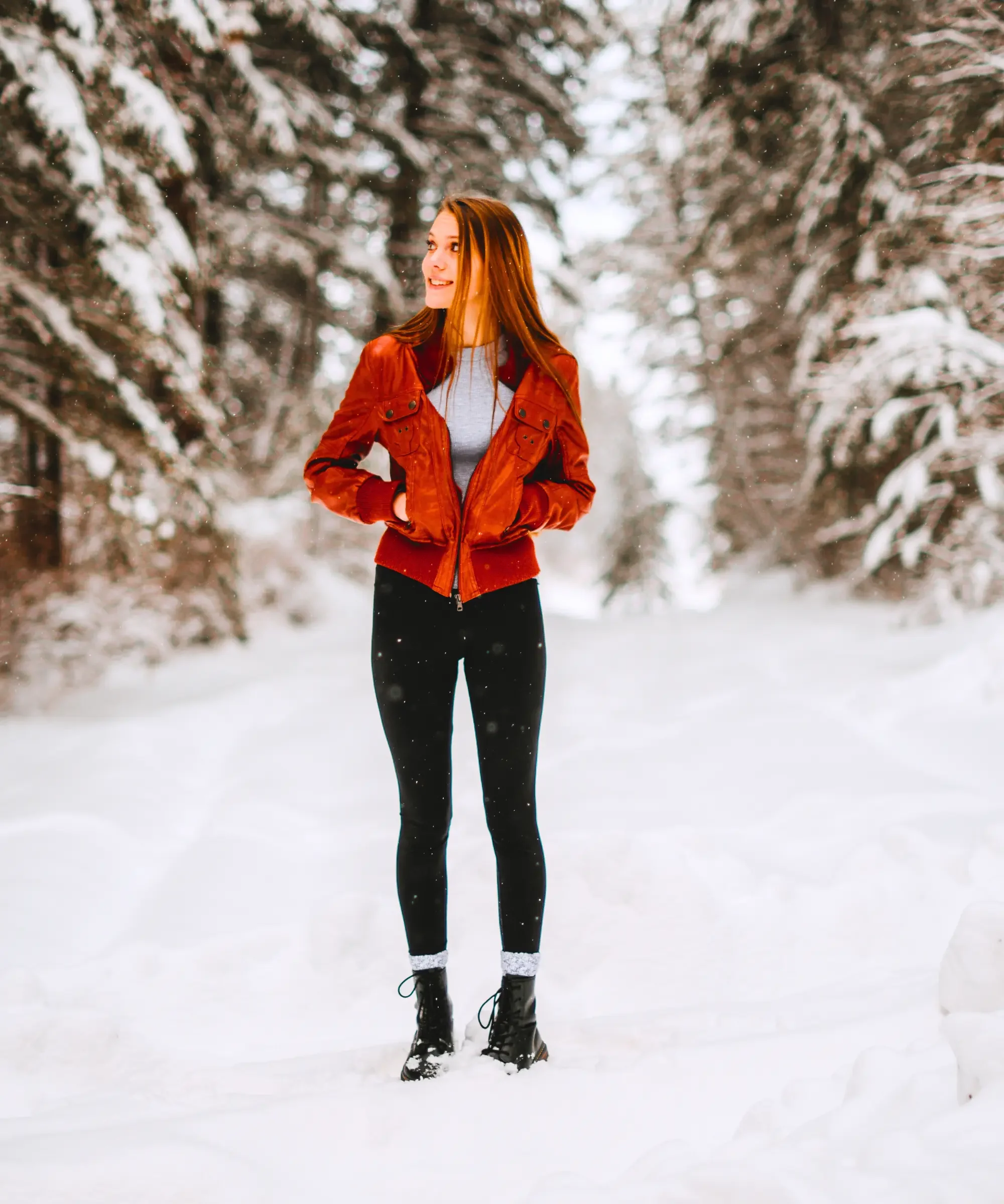 Woman wearing black winter leggings and boots standing in a snowy forest during winter.