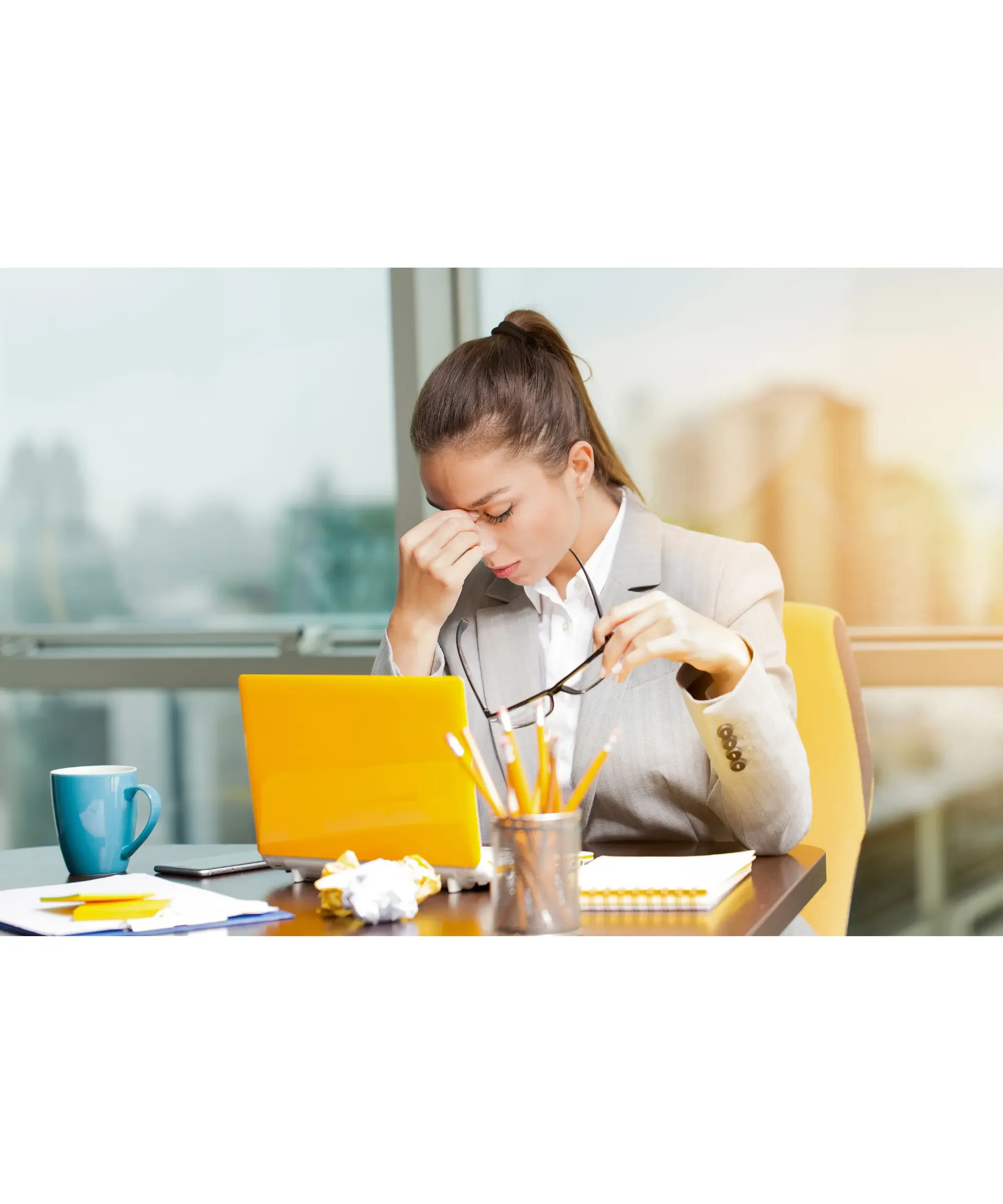 Stressed businesswoman sitting at desk with laptop holding glasses and rubbing eyes showing work burnout and fatigue