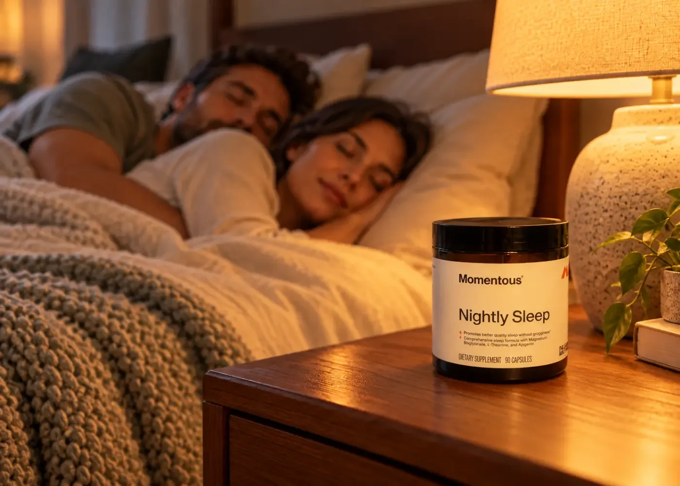 A couple sleeping in a warmly lit bedroom, with a Momentous Nightly Sleep bottle on the bedside table.