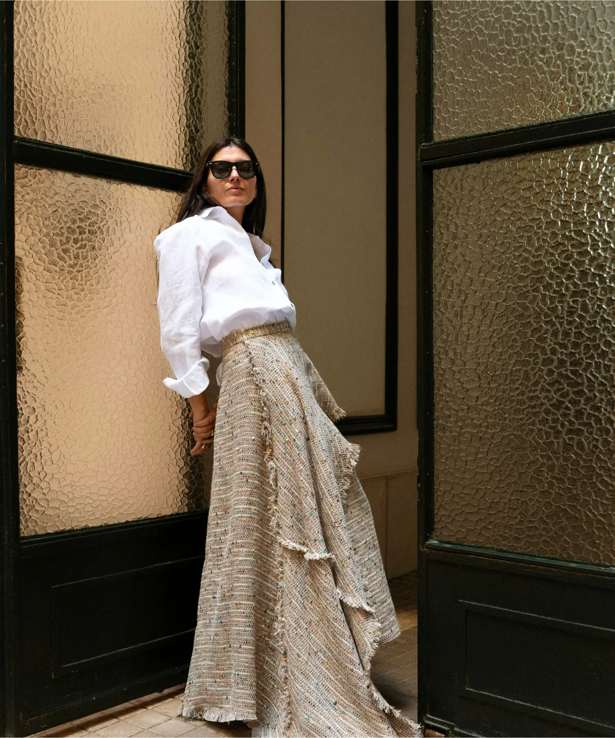 Woman standing confidently in a white blouse and textured skirt, representing a reflective personal lifestyle moment