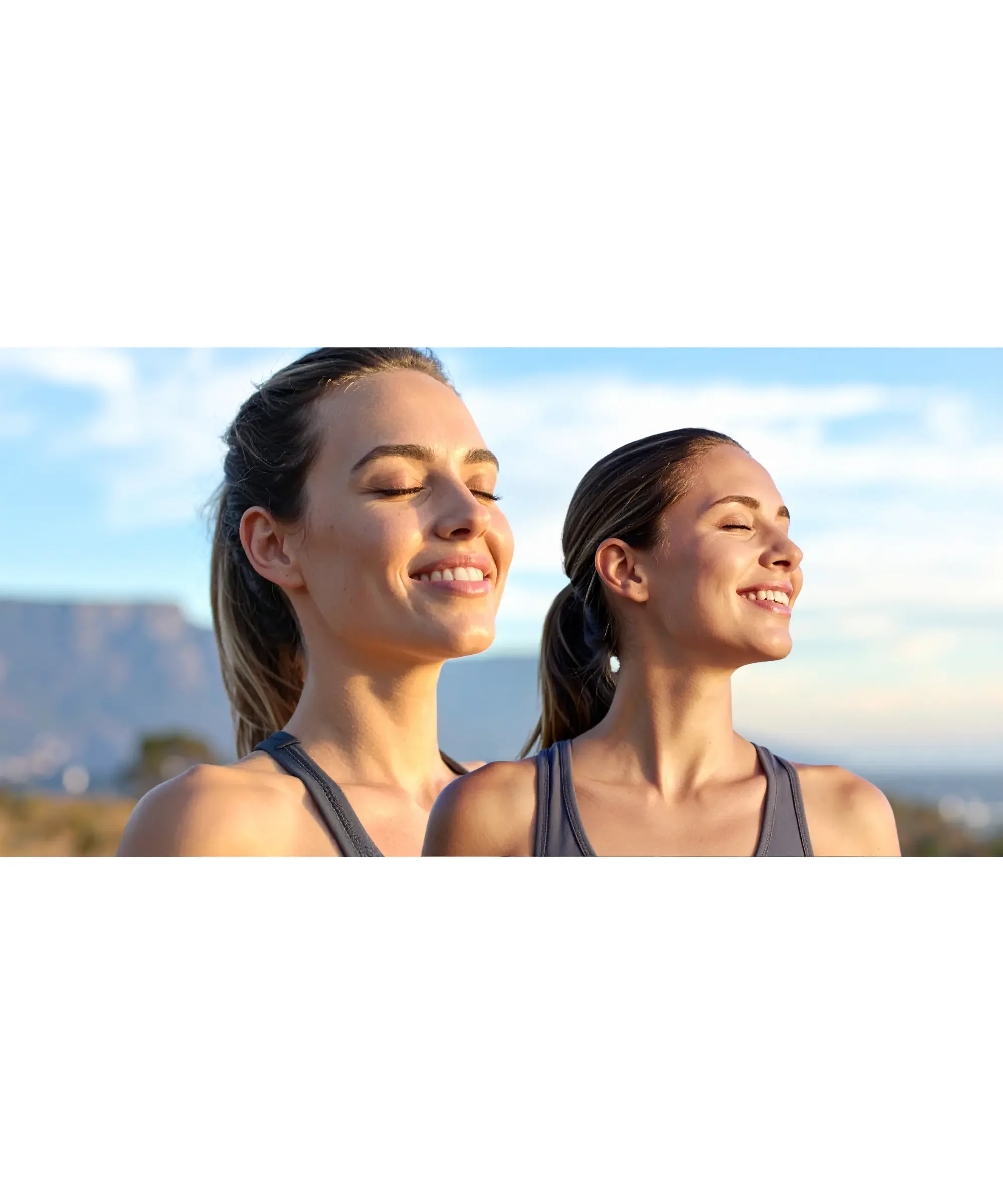 Two women with eyes closed enjoying deep breathing outdoors in sunlight, calm expression, wellness and stress relief concept, mindful breathing and relaxation in nature