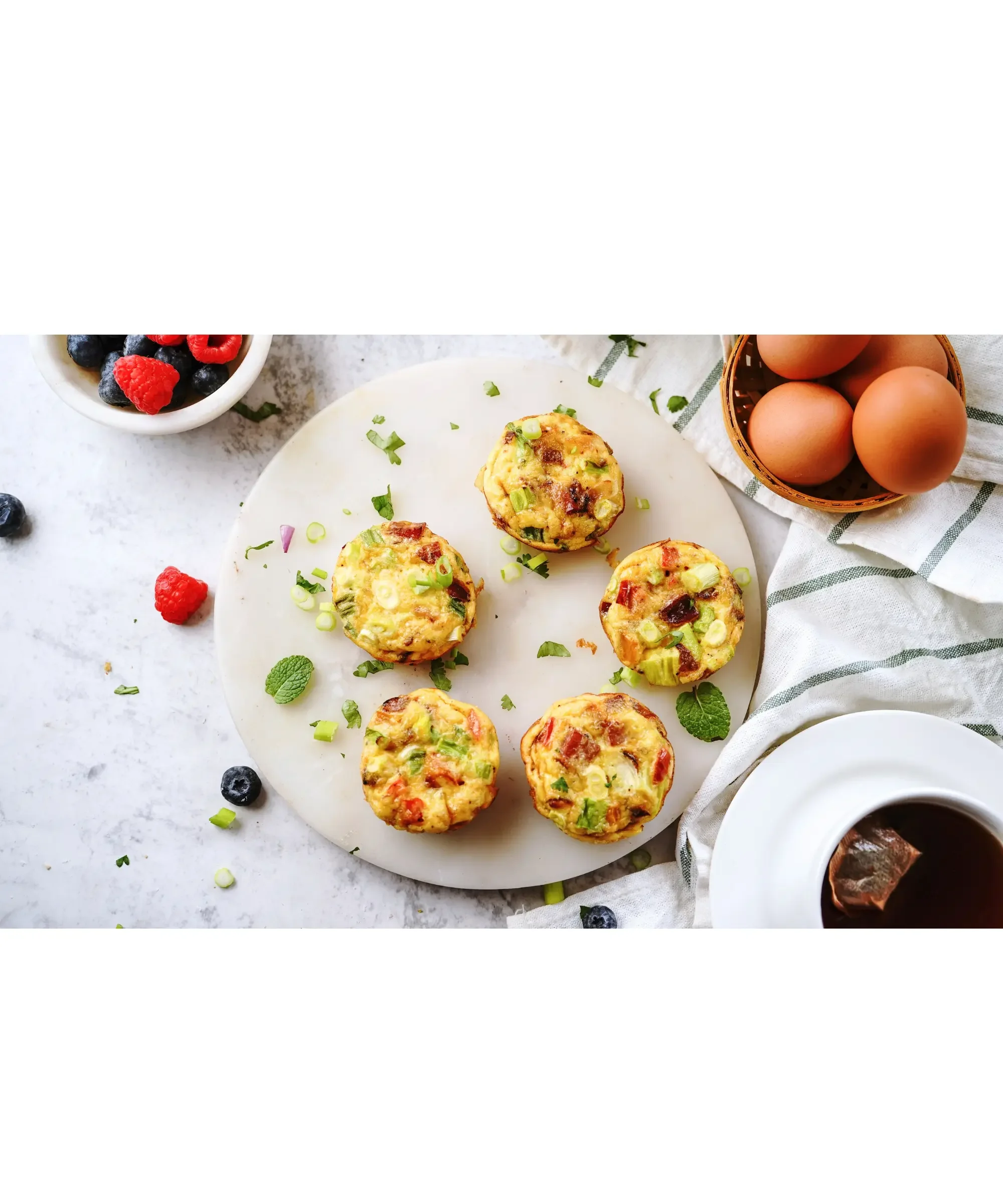 Egg muffins with vegetables arranged on a plate, surrounded by fresh ingredients