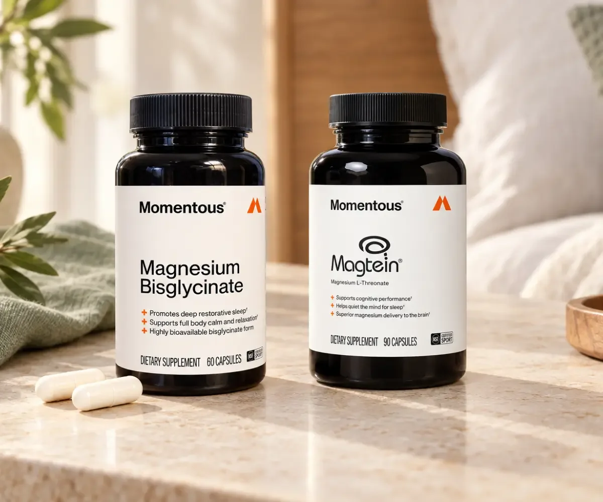 Two Momentous magnesium supplement bottles—Magnesium Bisglycinate and Magtein Magnesium L-Threonate—displayed with two white capsules on a warm bedside table with soft natural light.