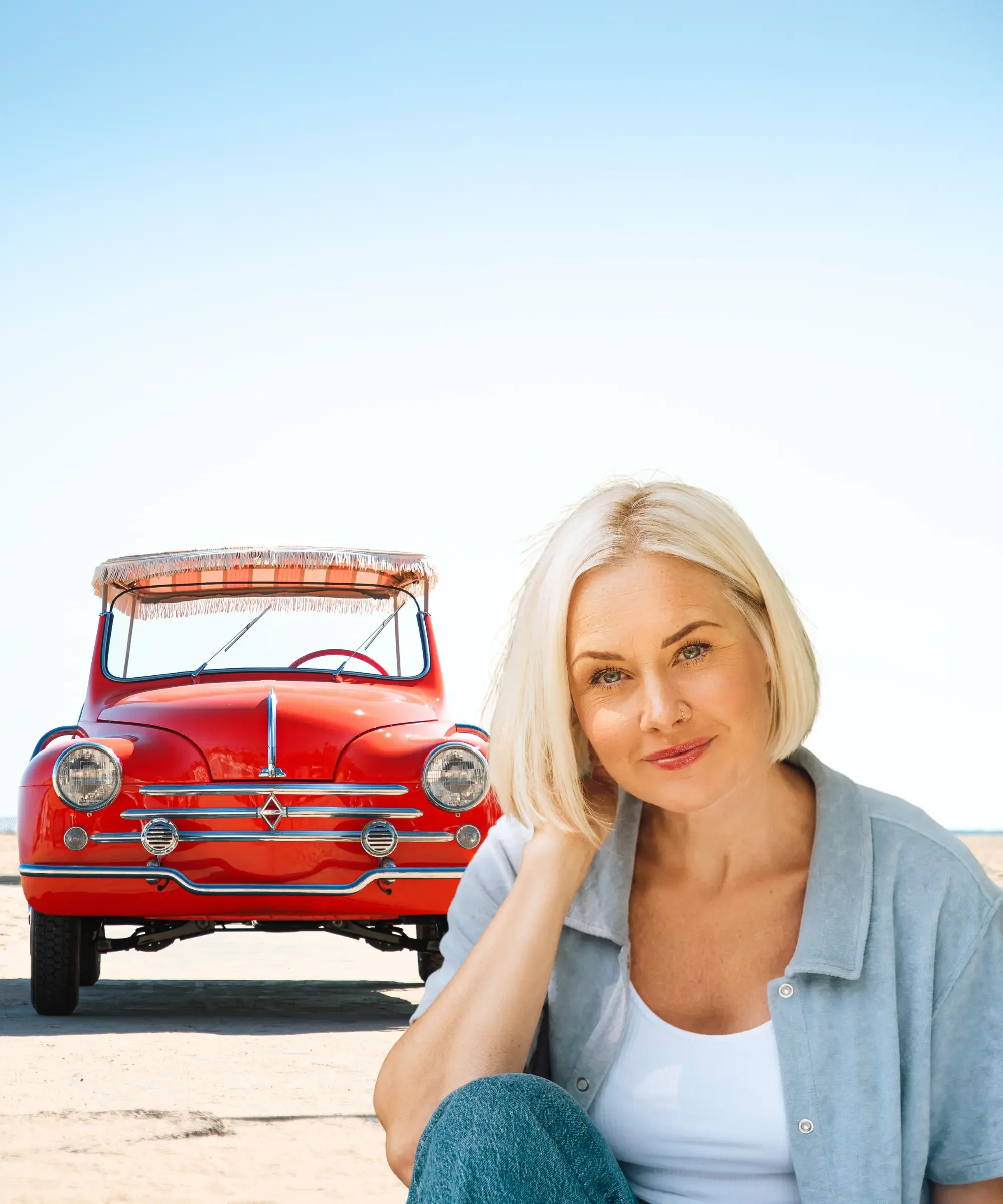 Confident woman over 40 sitting outdoors with a vintage red car, symbolizing midlife reinvention, calm confidence, and a fresh chapter in life.