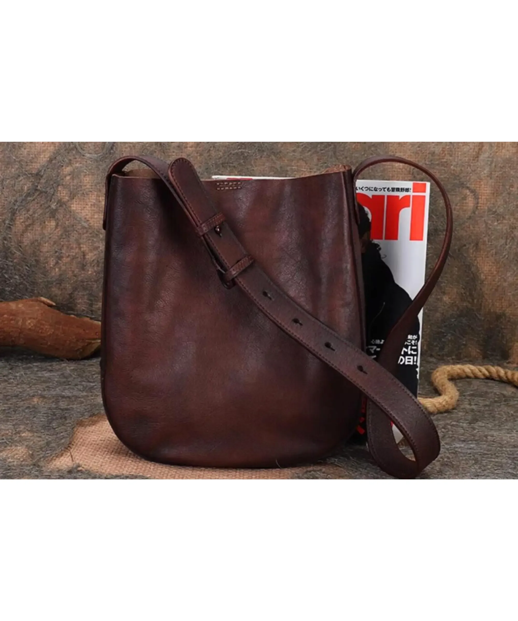 Top grain leather handmade crossbody bag in a rich vintage brown finish, featuring an adjustable shoulder strap and a structured yet soft silhouette, styled with a magazine for scale against a textured backdrop.