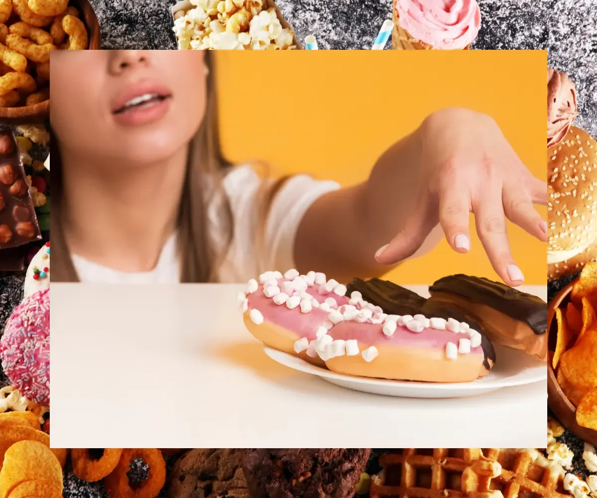Woman reaching for frosted doughnuts surrounded by assorted sugary and processed foods.