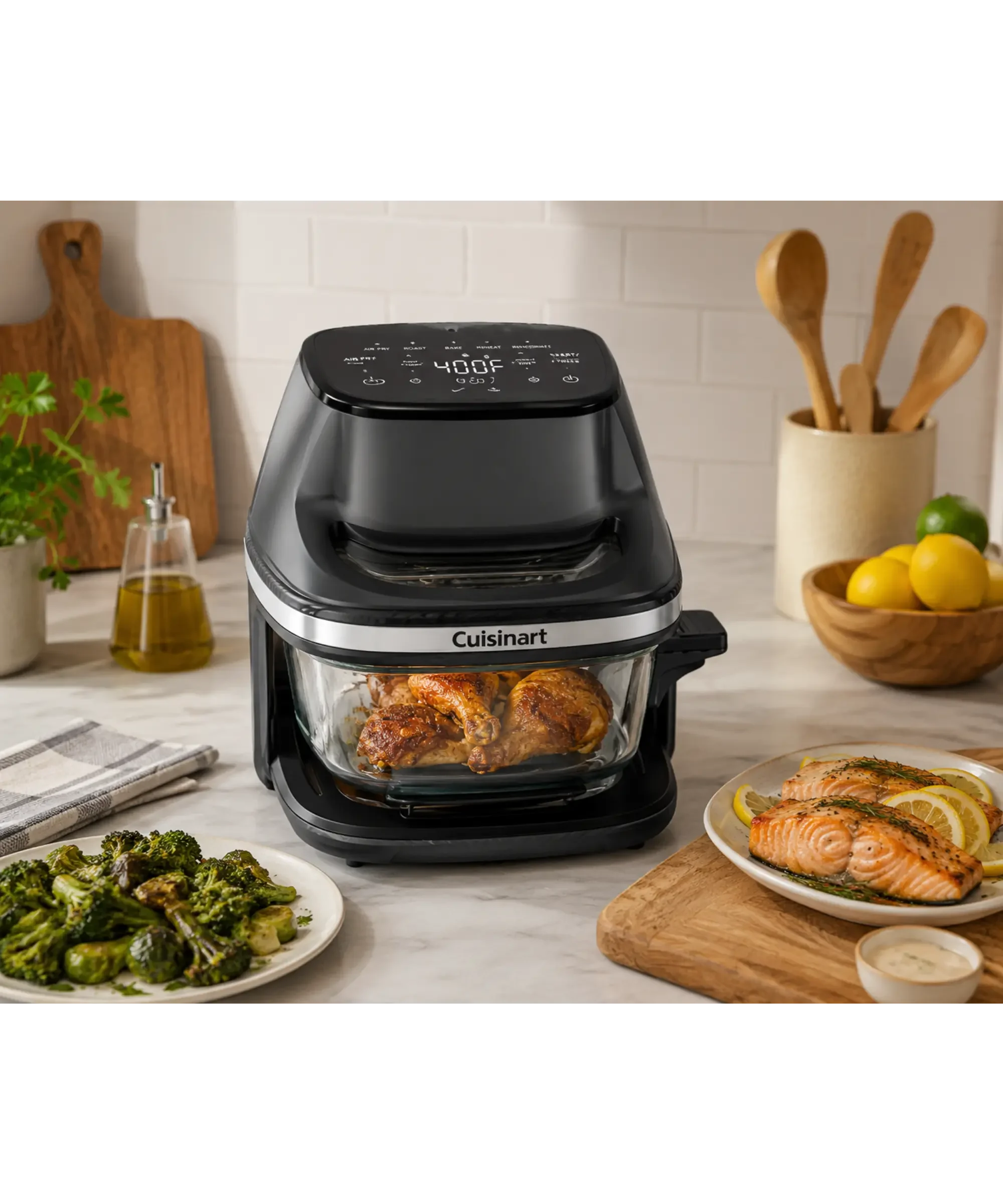 Black Cuisinart air fryer with a clear glass cooking basket displayed on a bright kitchen countertop beside roasted chicken, salmon, vegetables, and fresh lemons, showcasing its modern design and easy food visibility.