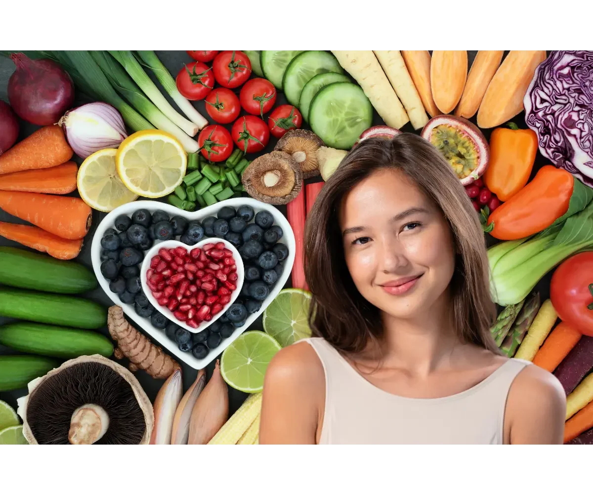 Smiling woman surrounded by colorful fruits and vegetables, including berries, tomatoes, cucumbers, carrots, and peppers.