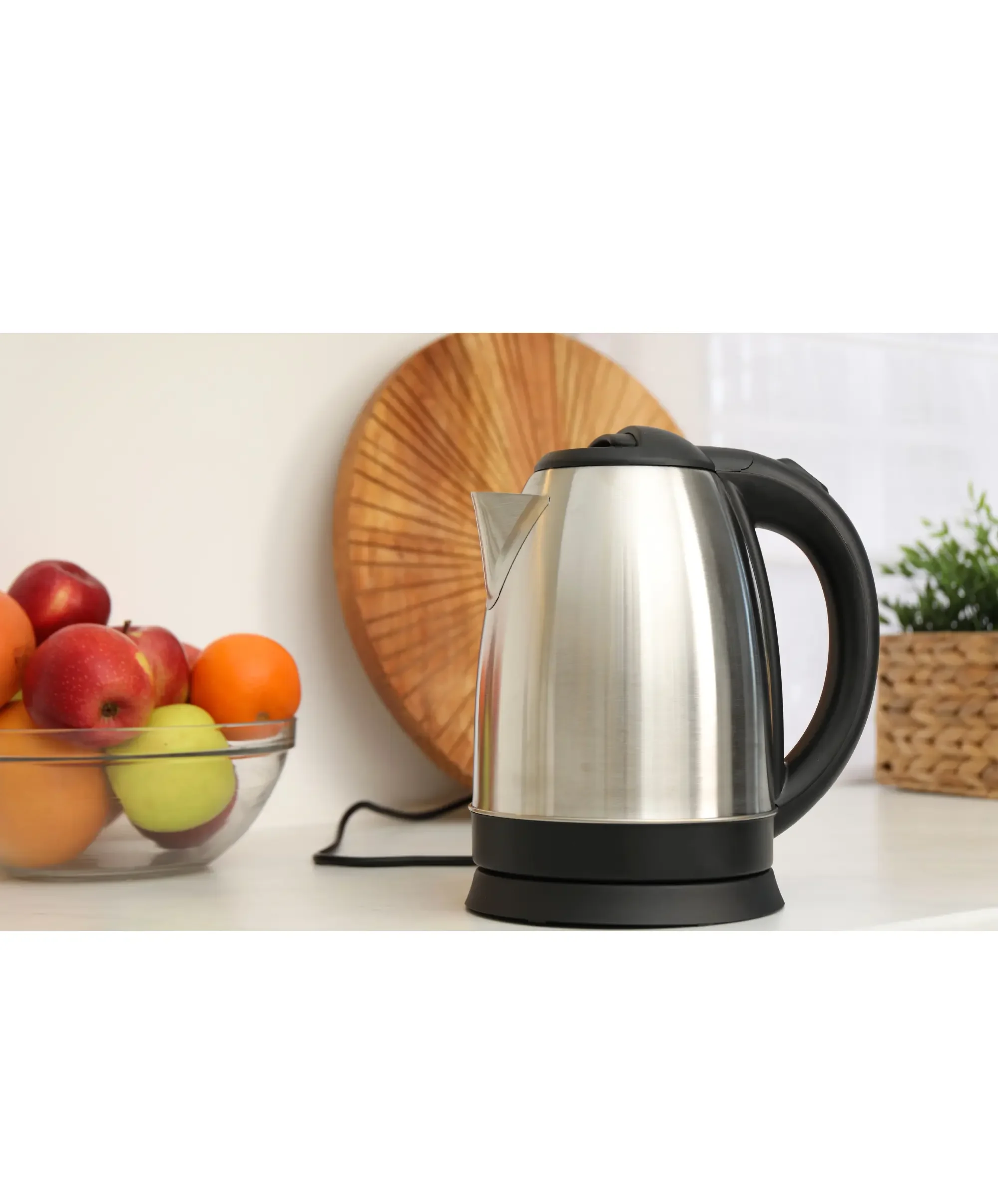 Stainless steel kettle over a counter top with fruits on the side and a plant