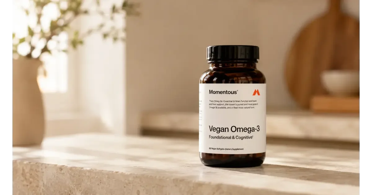 Momentous Vegan Omega-3 supplement bottle on a light stone countertop in a warm, sunlit kitchen.