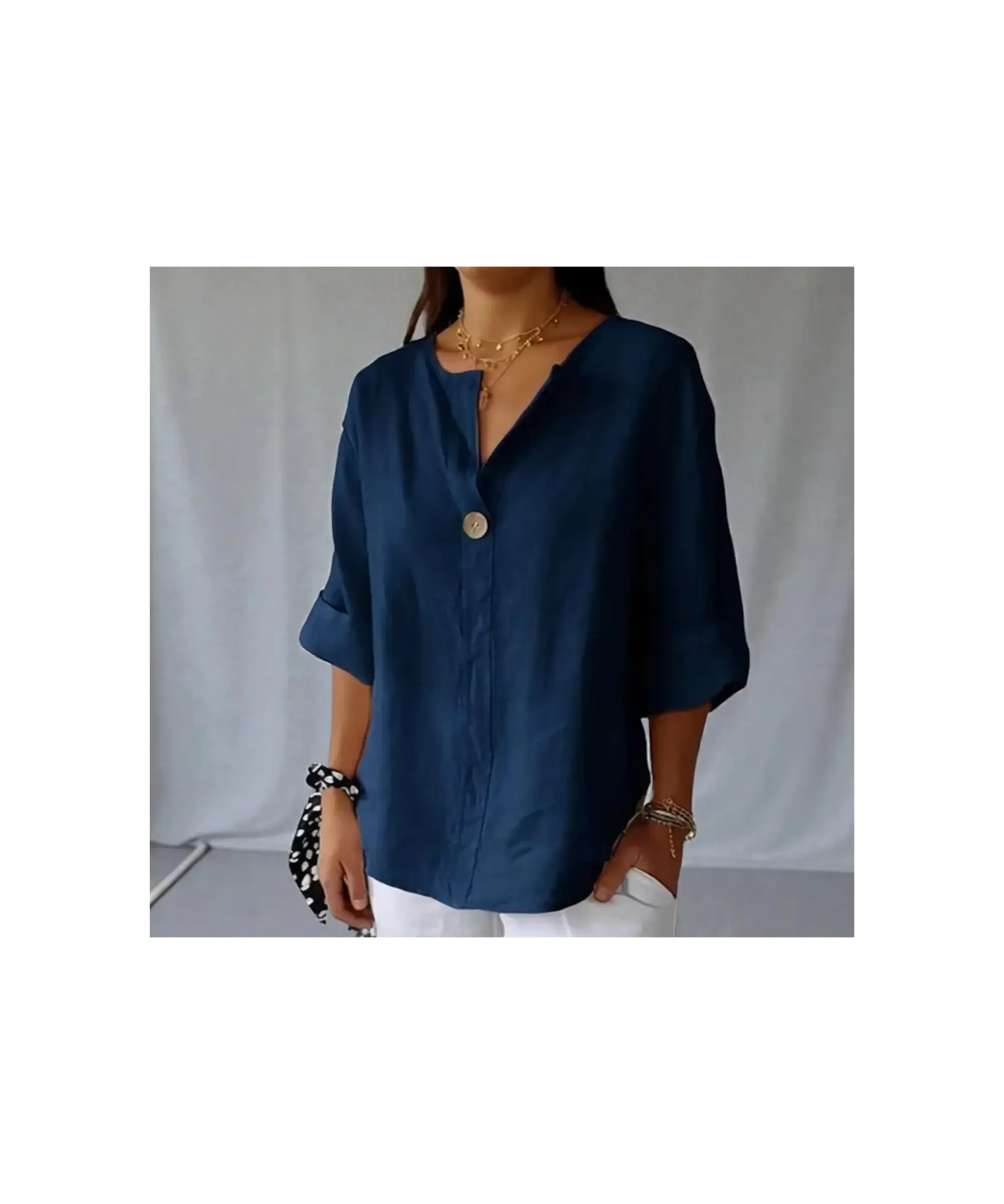 Navy blue oversized linen V-neck blouse with a loose, relaxed fit and short rolled sleeves, styled with white pants and layered gold jewelry in a soft, minimalist setting.