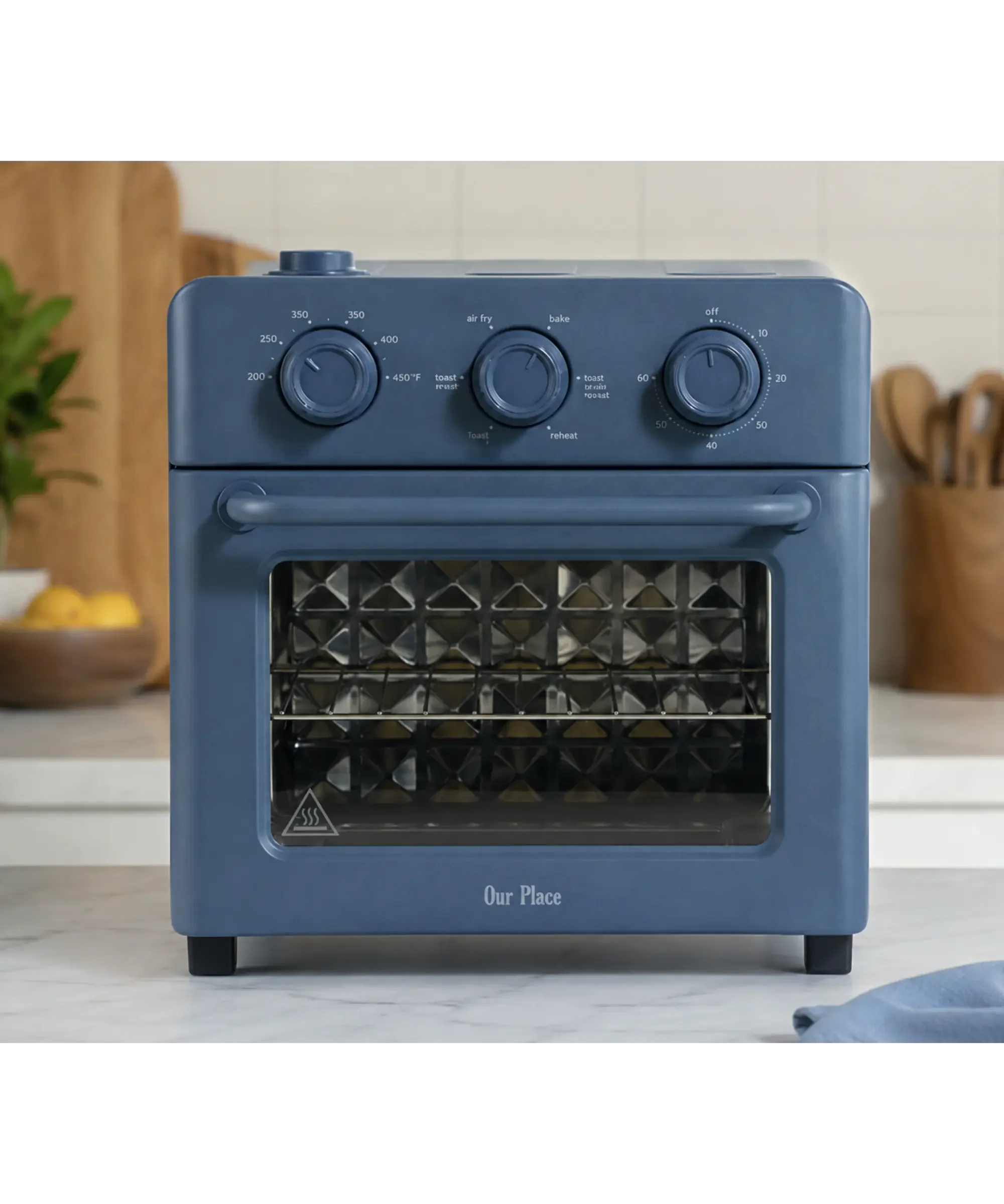 Blue Our Place air fryer with a retro-inspired design displayed on a bright marble countertop in a modern kitchen, highlighting its non-toxic cooking surface and compact countertop size.