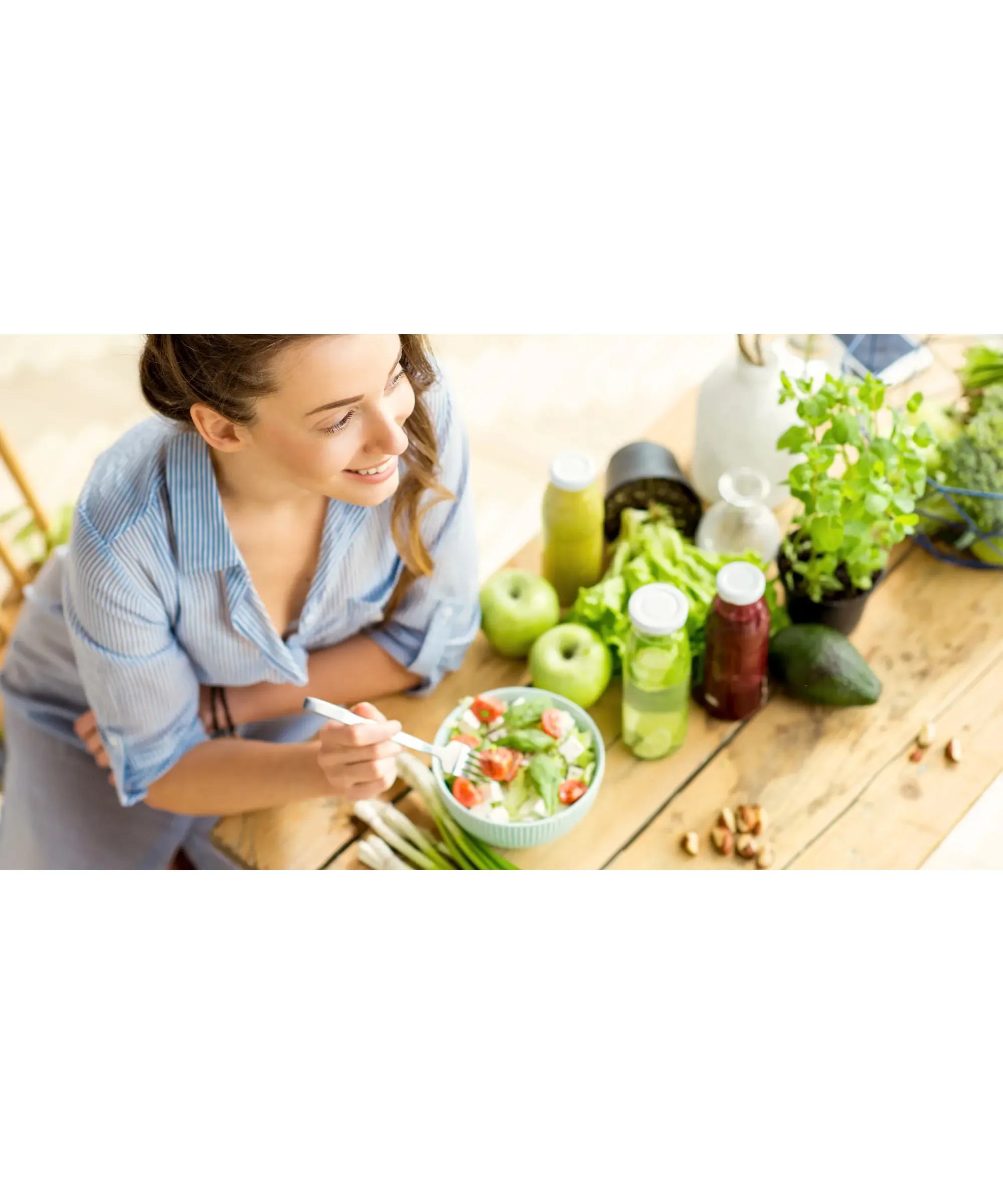 Smiling woman enjoying a fresh green salad with vegetables at a bright kitchen table — concept of healthy eating for reducing inflammation.