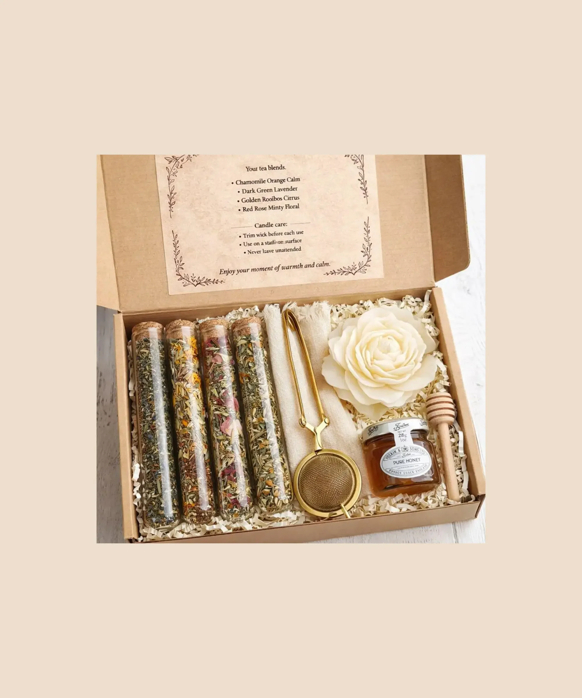 Herbal tea gift set with artisan loose-leaf tea blends, honey jar, tea infuser, candle, and wooden honey dipper arranged in a gift box.