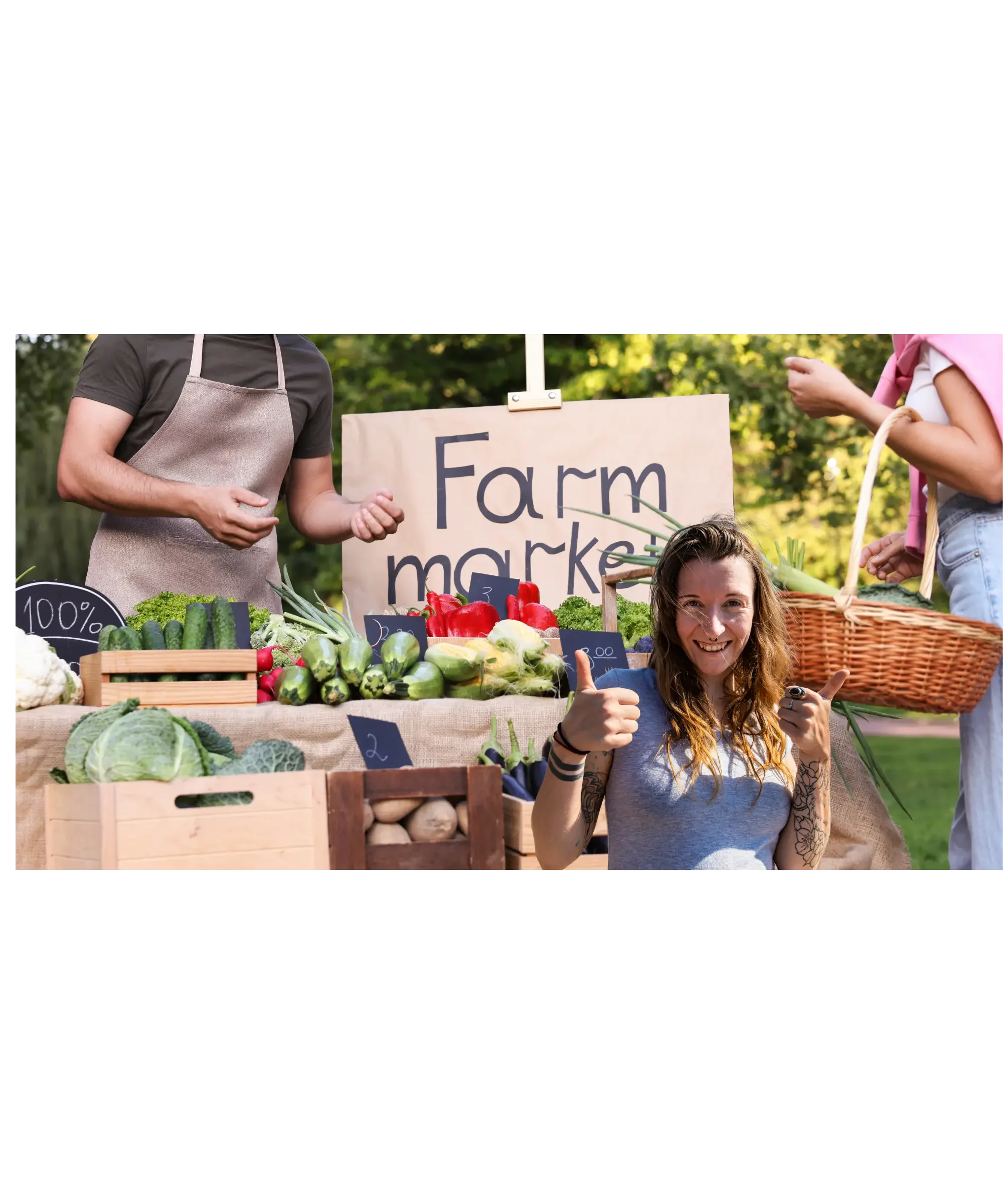 Smiling woman giving a thumbs-up at a farmers market stand filled with fresh vegetables, with vendors and a “Farm market” sign in the background.