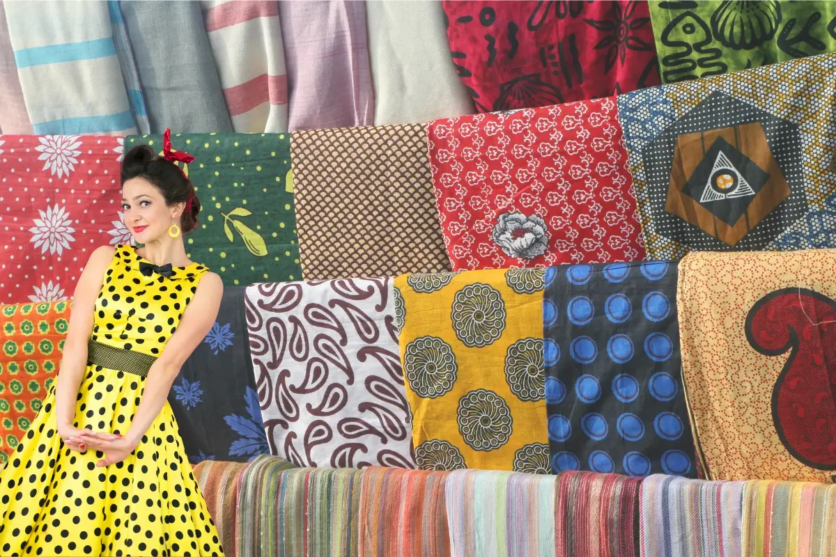 Woman in a yellow polka-dot dress posing in front of colorful textile fabrics, representing fashion sourcing and textile options in China.
