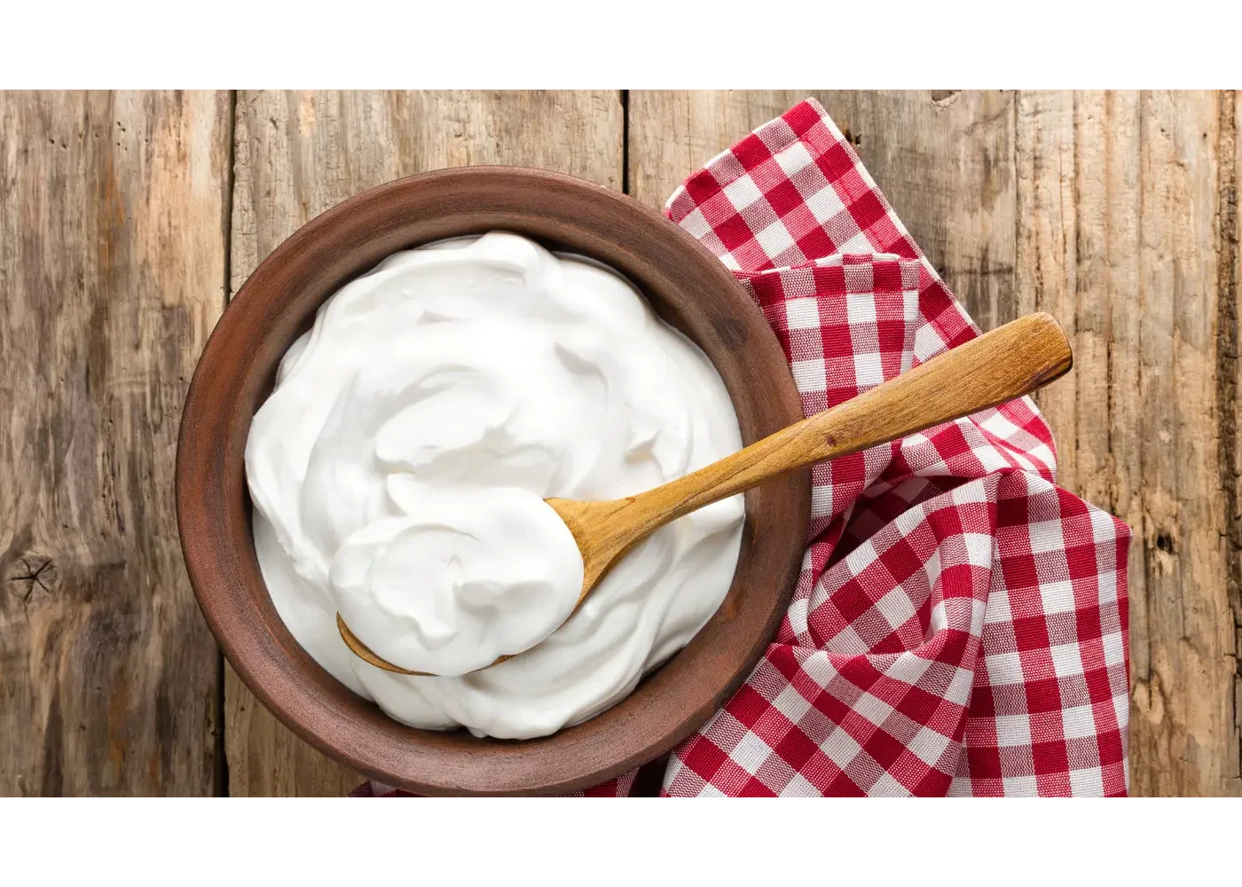 bowl of yogurt with a wood spoon over a wood table and a red napkin
