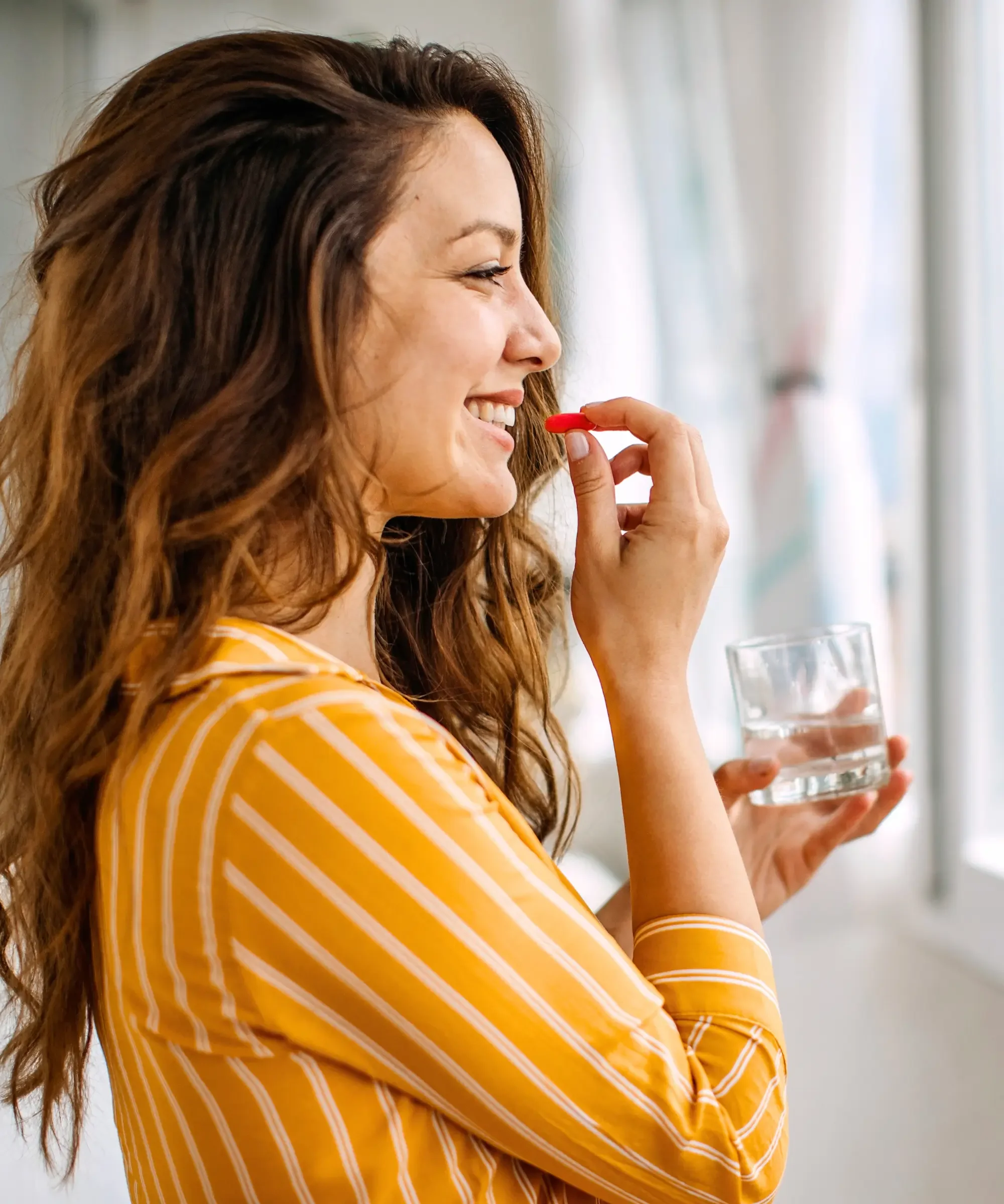 Woman taking a supplement capsule with water, representing daily wellness habits and supplement use