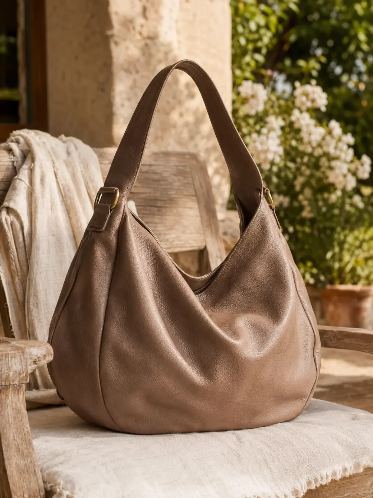 Taupe leather hobo bag with a soft, slouchy shape displayed on a chair in a sunlit garden.